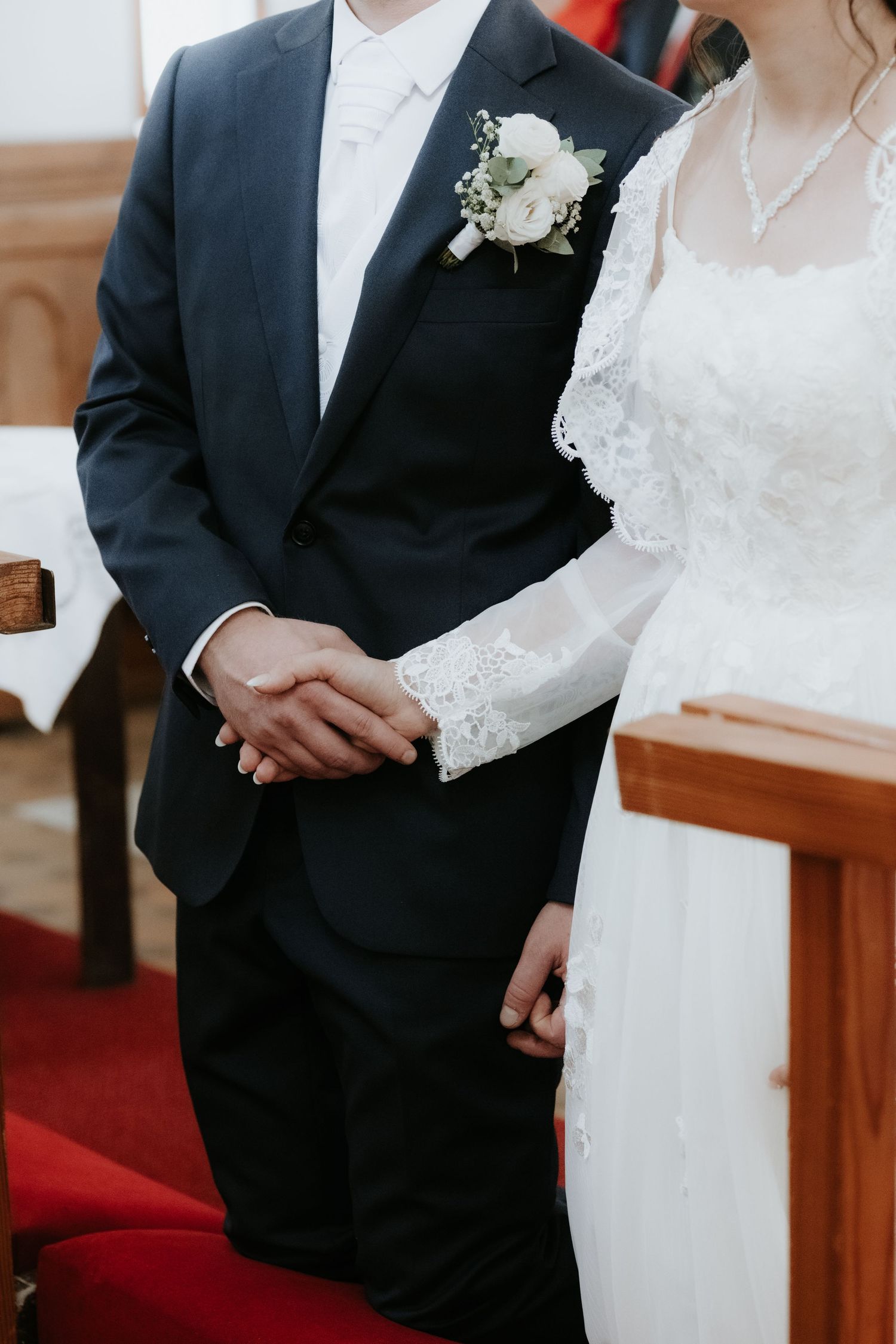 Bride and groom holding hands at altar, groom in navy suit with white boutonniere.