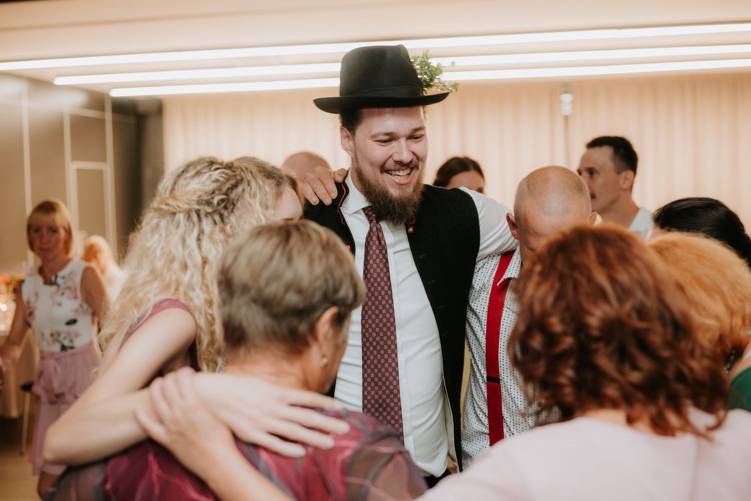 Man in black hat and tie dancing with guests at a wedding reception celebration.