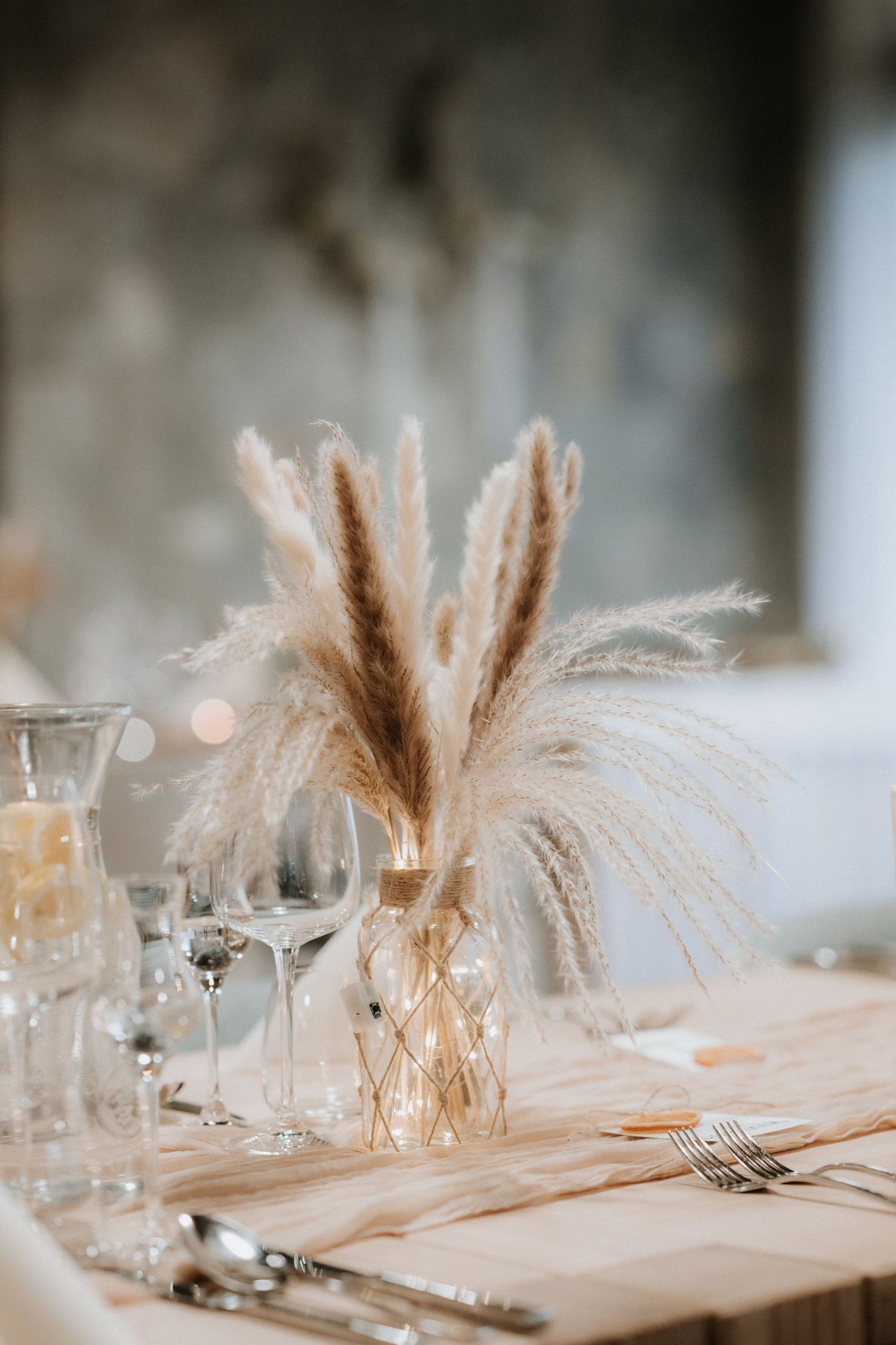 Elegant boho wedding table setting with pampas grass centerpiece, crystal glasses, and neutral linen decor.
