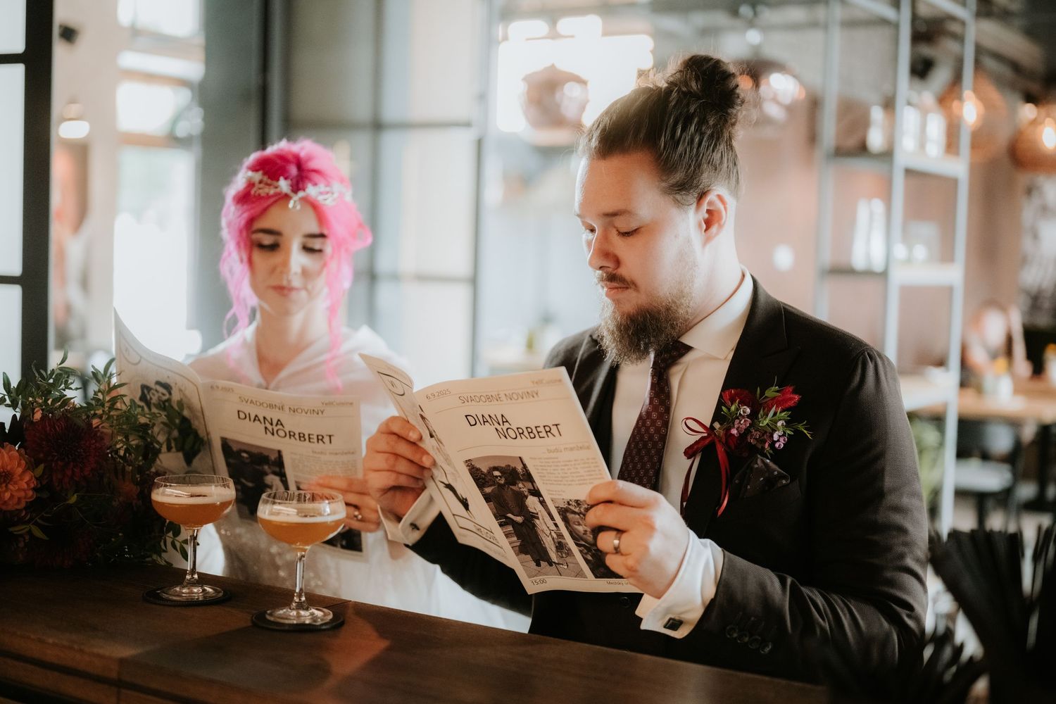 Bride with pink hair and groom in suit reading wedding newspapers at a bar with craft beers.