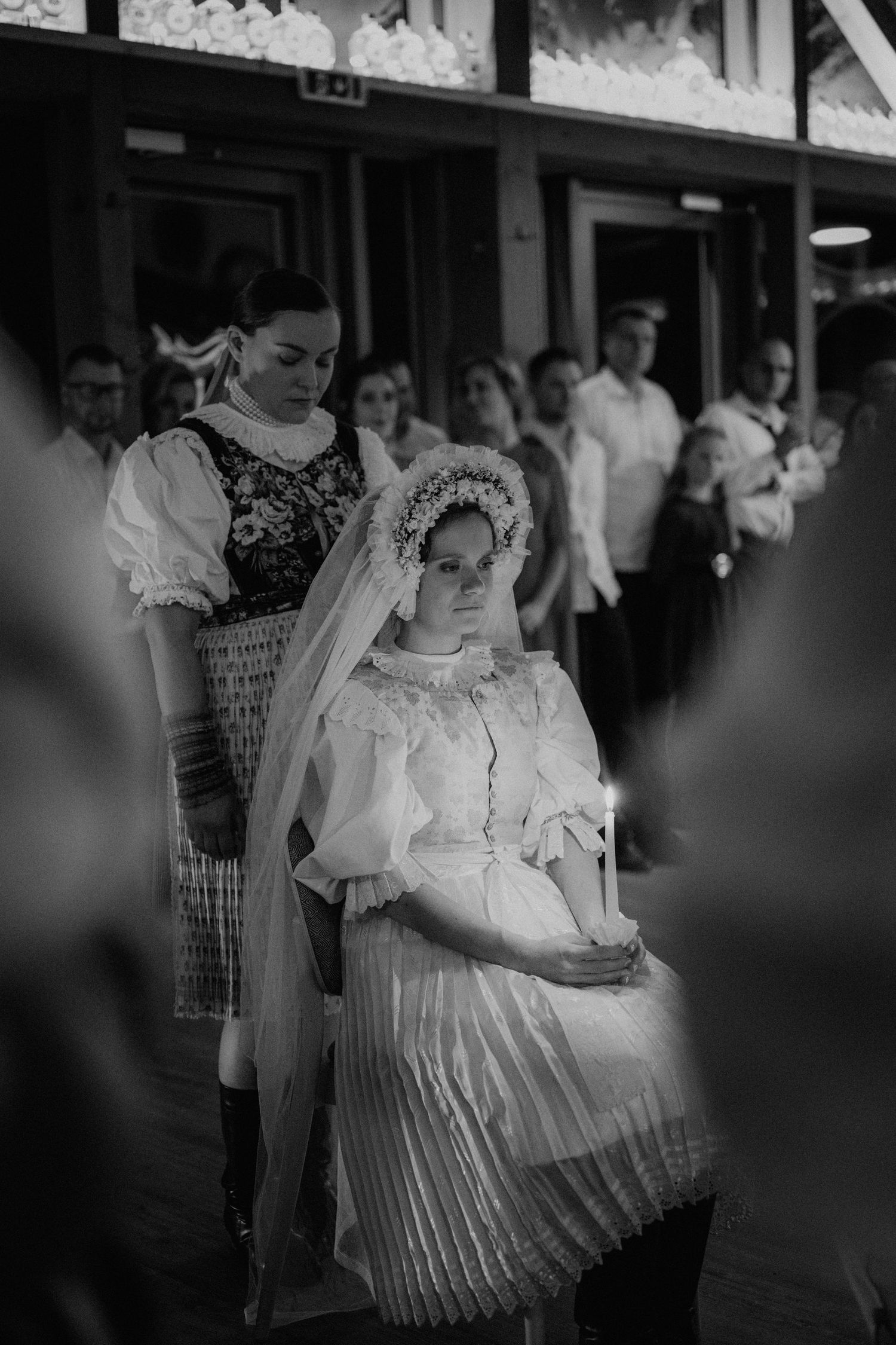 Black and white photo of a bride in traditional folk costume holding a candle during a wedding ceremony.