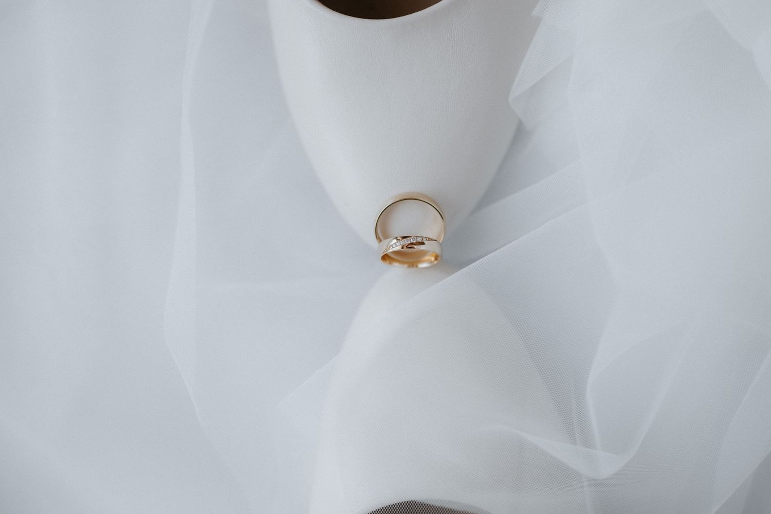 Two gold wedding rings resting on soft white bridal veil fabric.