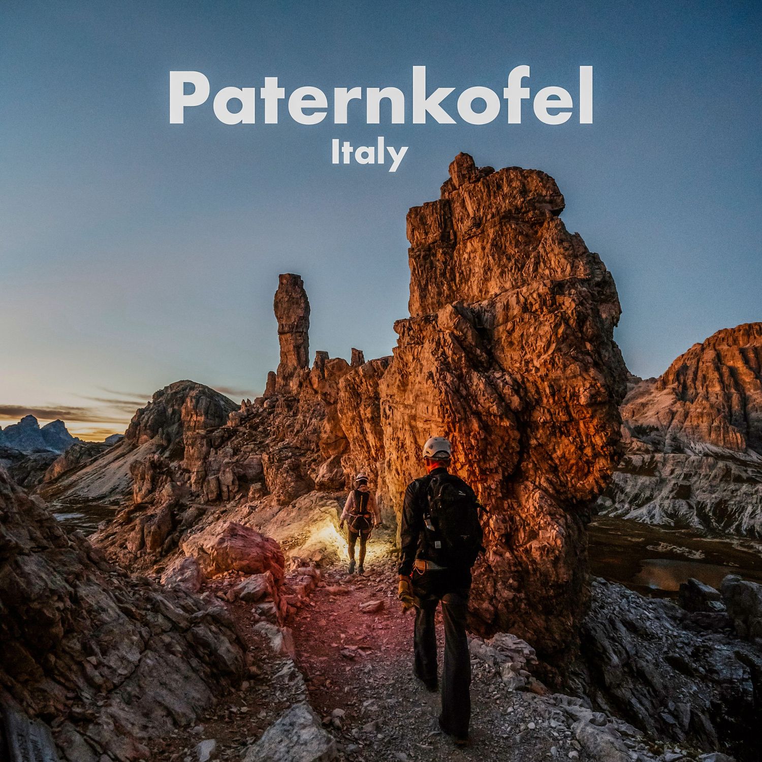 Two hikers explore the dramatic rocky spires of Paternkofel mountain in the Dolomites, Italy, at dusk.