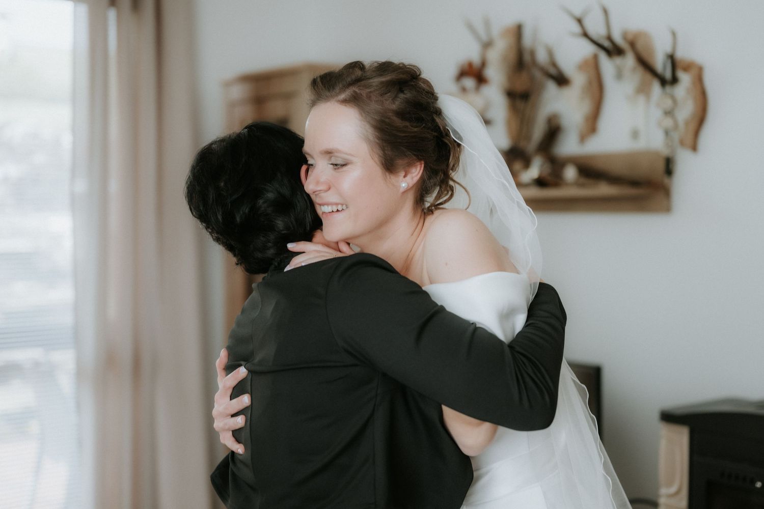 Bride in white wedding dress smiling and hugging a guest in a black suit during a wedding celebration.