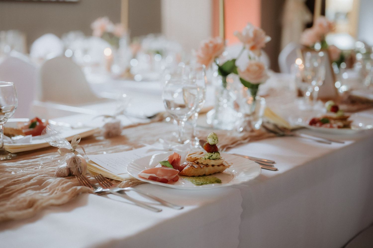 Elegant wedding reception table setting with white linens, crystal glasses, pink floral centerpieces, and plated appetizers.