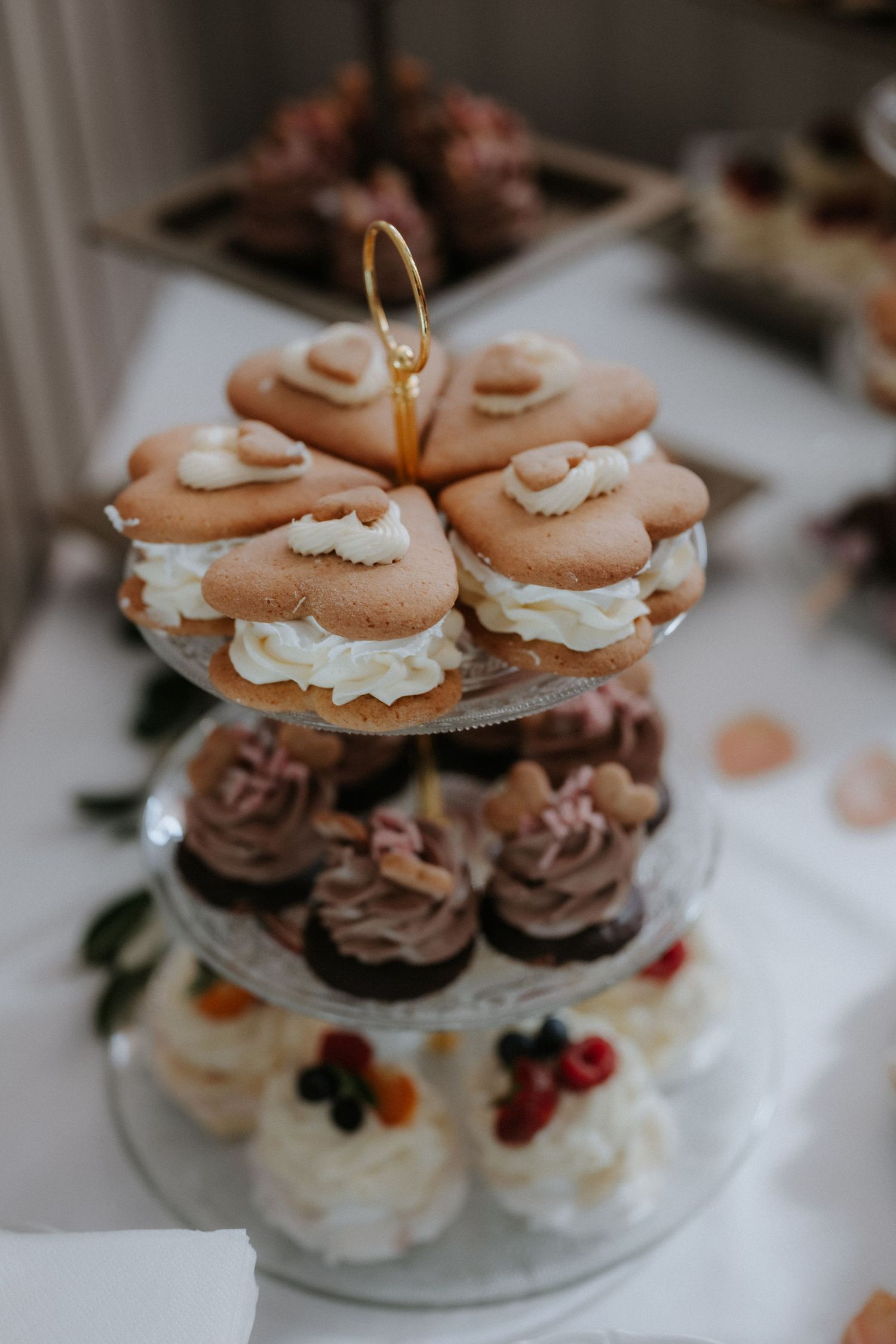 Three-tier dessert stand with macarons, chocolate cupcakes, and cream-topped mini cakes at an elegant event.