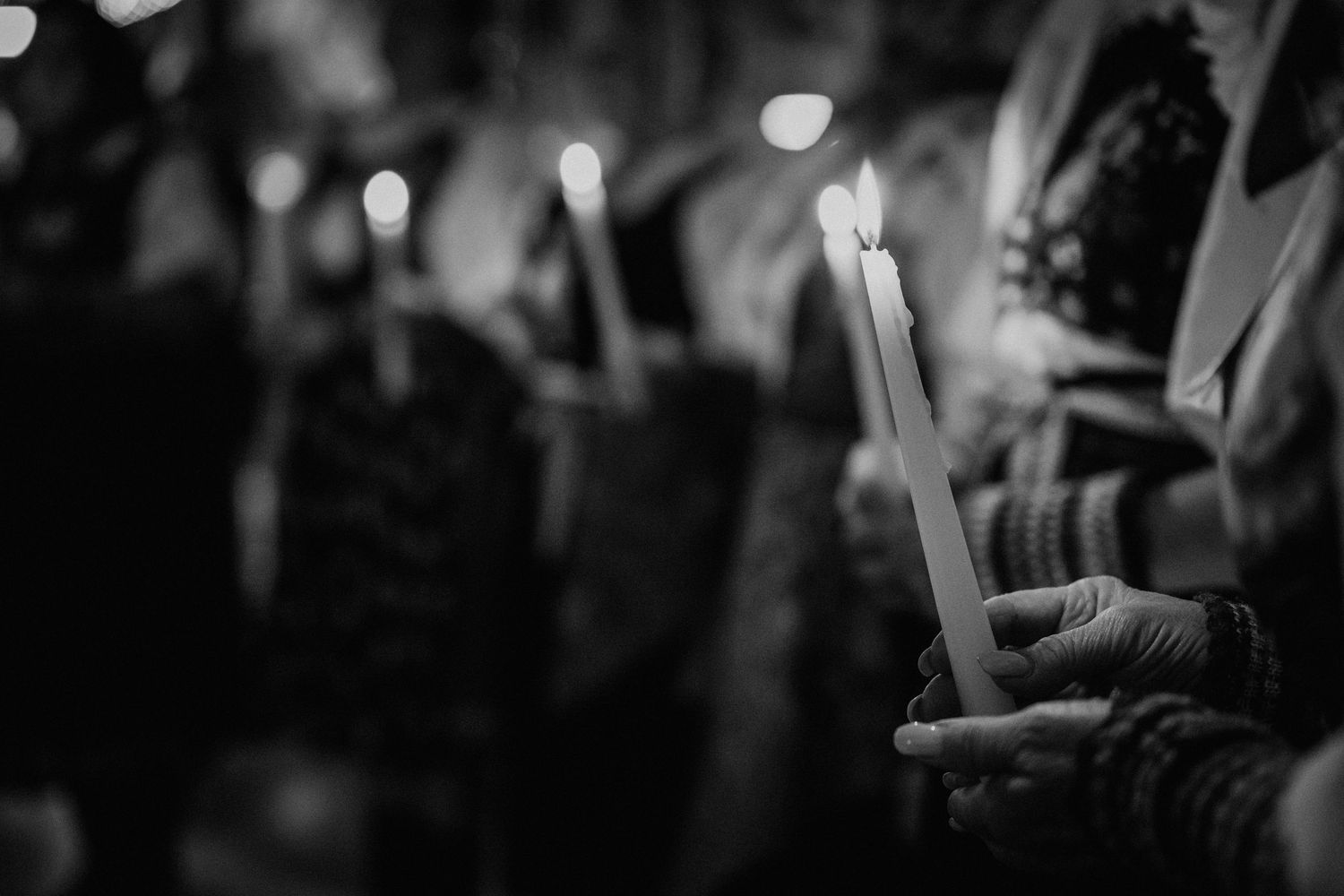 Black and white photo of hands holding a lit candle at a candlelight vigil ceremony.
