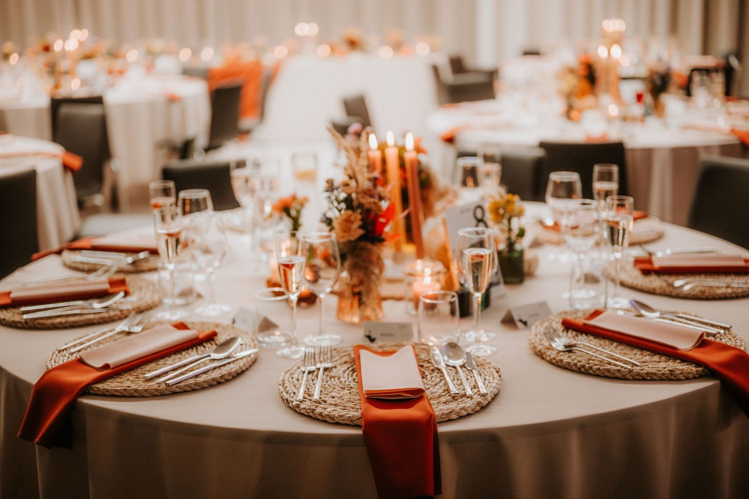 Elegant wedding reception tables with gray linens, burnt orange napkins, gold chargers, candles, and floral centerpieces.
