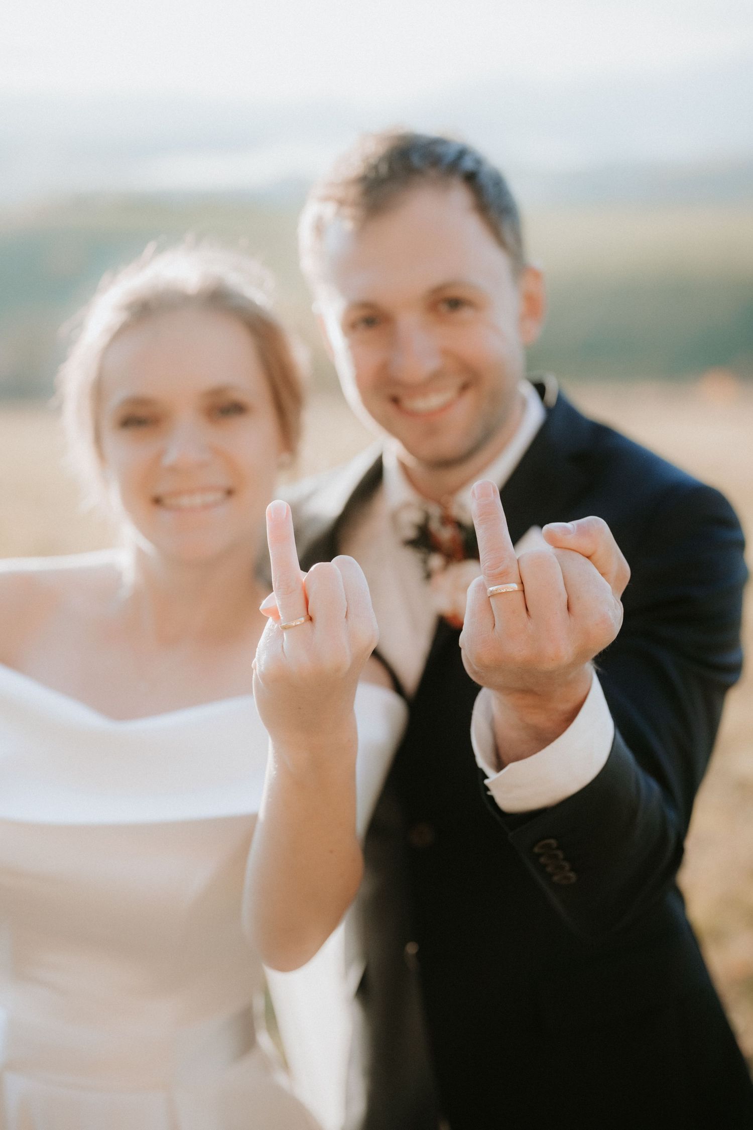 Smiling newlyweds in wedding attire showing off their wedding rings on their ring fingers outdoors.