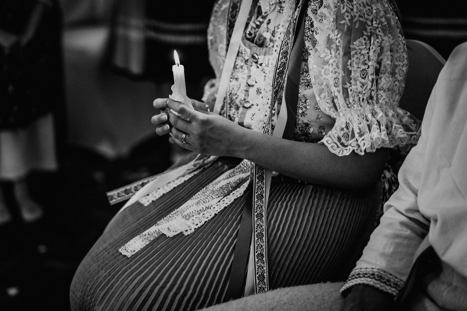 Pregnant woman holding a lit candle during a ceremony, wearing lace blouse, black and white photo.
