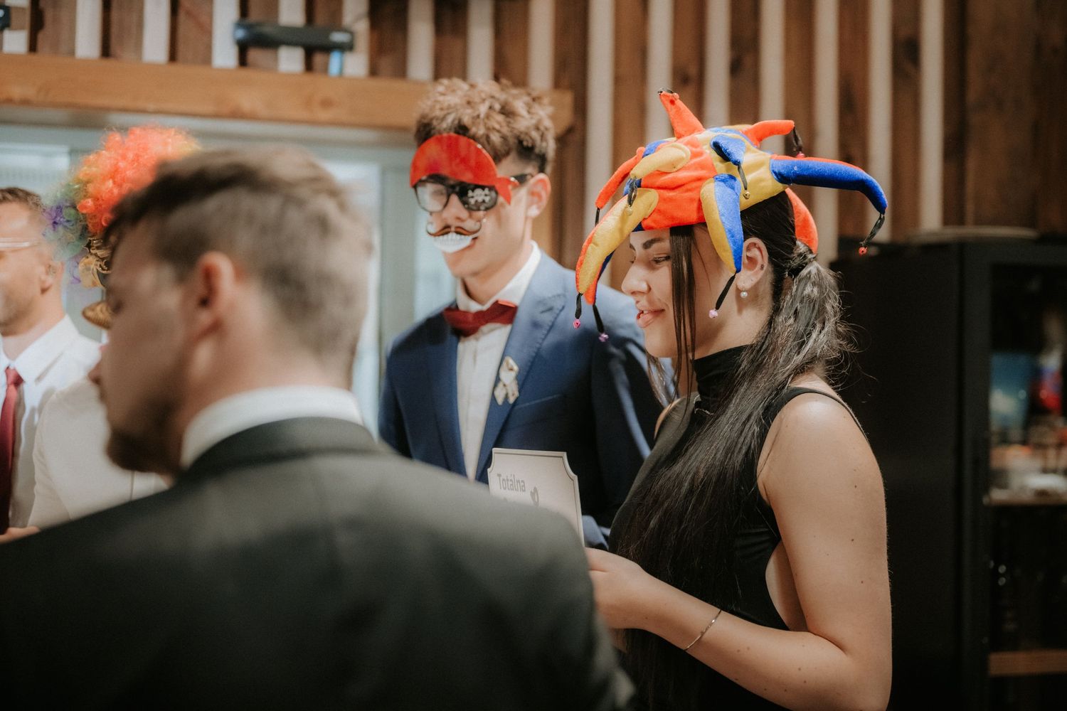 Guests wearing colorful masquerade masks at a festive party event in a rustic venue.