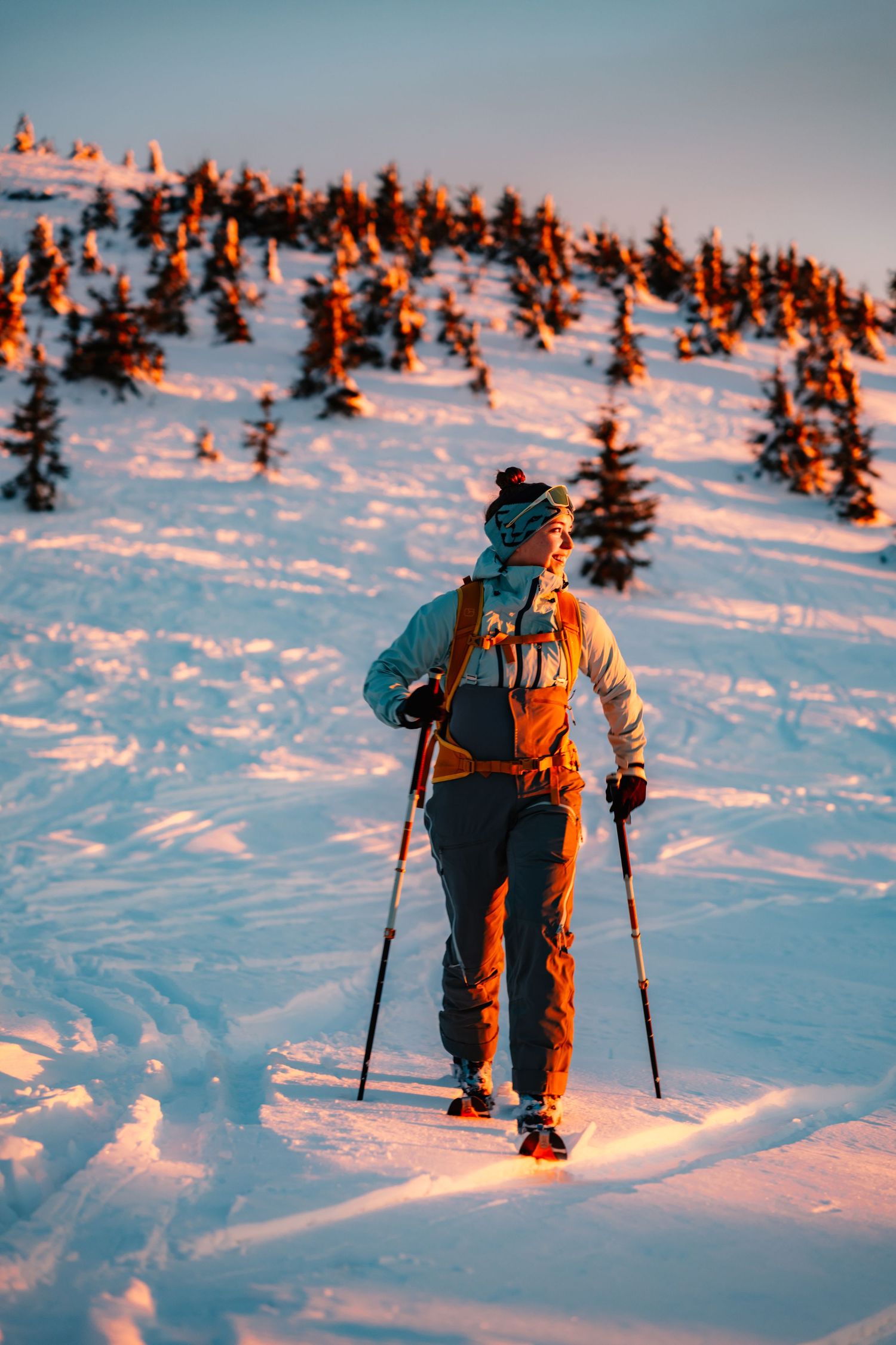 A hiker with poles and backpack snowshoeing up a snowy mountain slope at golden sunset.