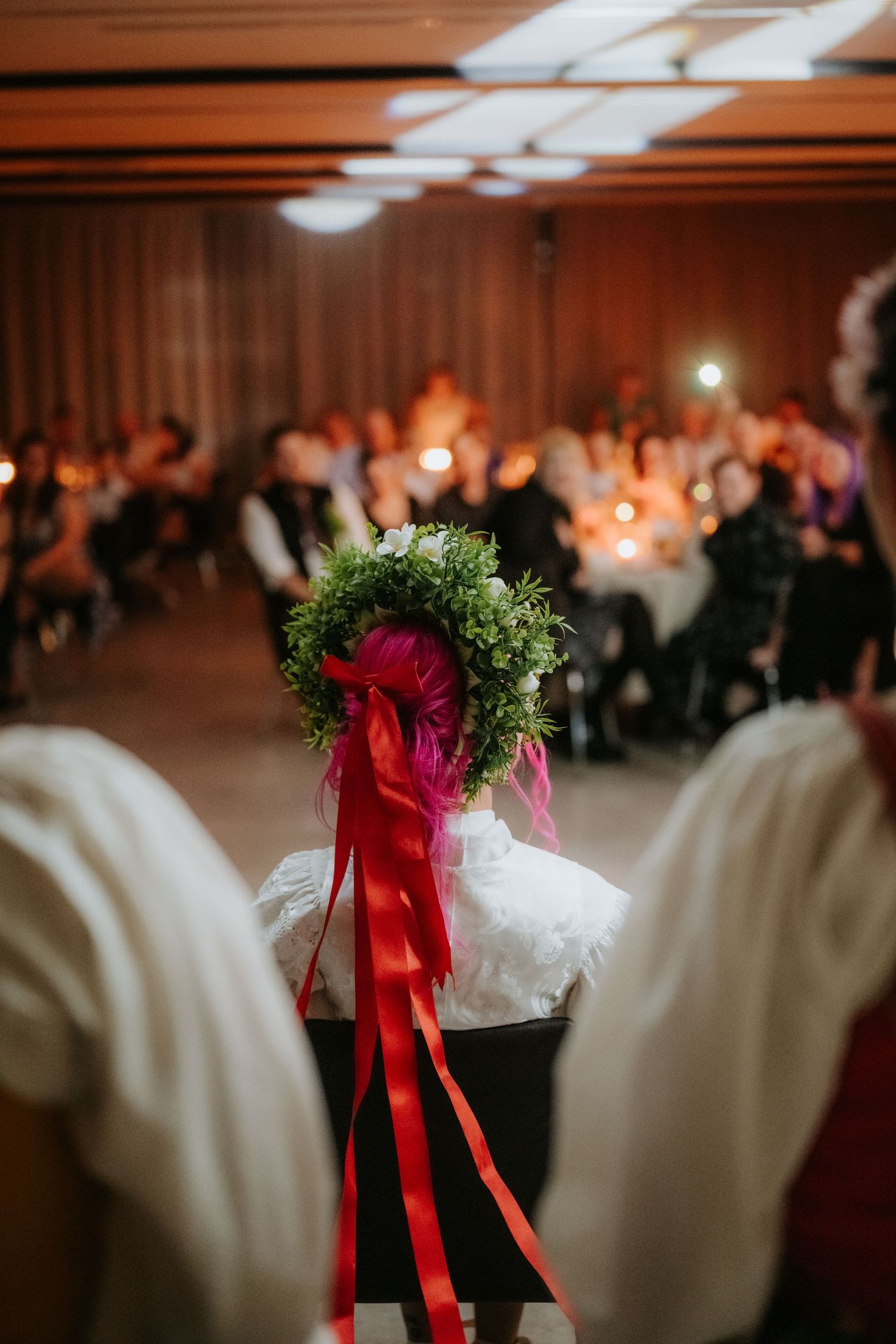 Bride wearing green floral crown with red ribbons at elegant candlelit wedding reception ceremony.