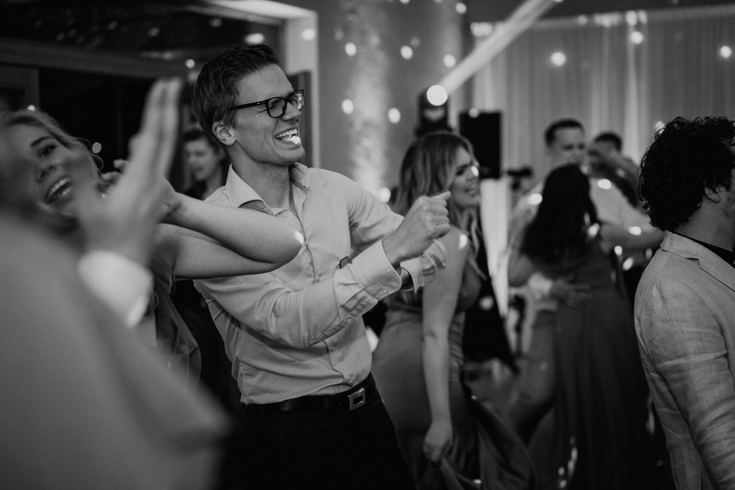 Black and white photo of guests laughing and dancing joyfully at a wedding reception party.