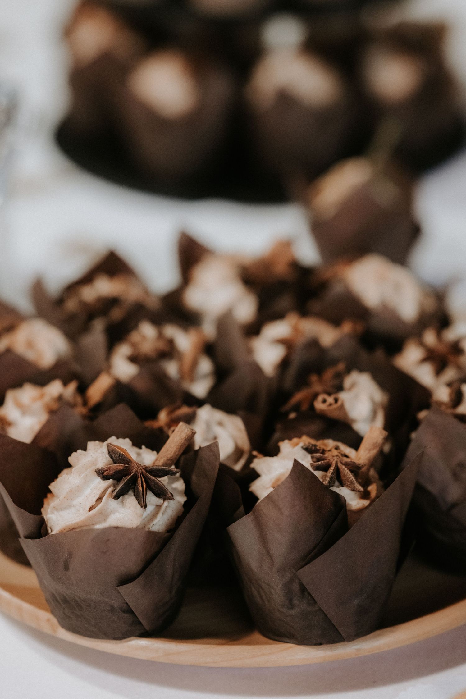 Chocolate cupcakes with whipped cream frosting and star anise spice in dark brown paper wrappers on a plate.