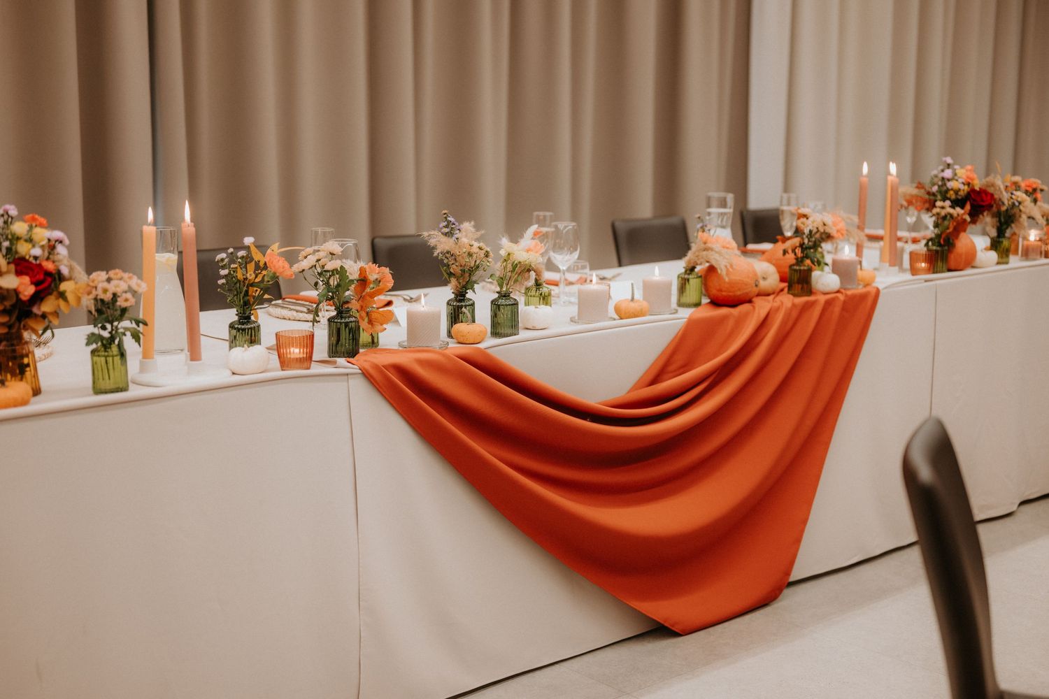 Wedding head table decorated with orange draped fabric, candles, and colorful floral arrangements for a fall celebration.