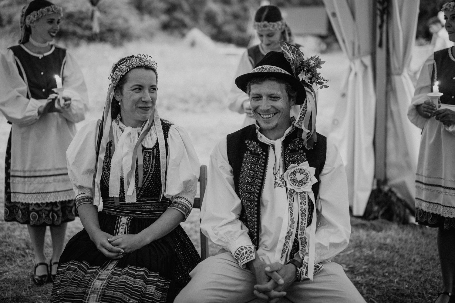 Two people in traditional folk costumes smile at a cultural celebration outdoors in black and white photo.