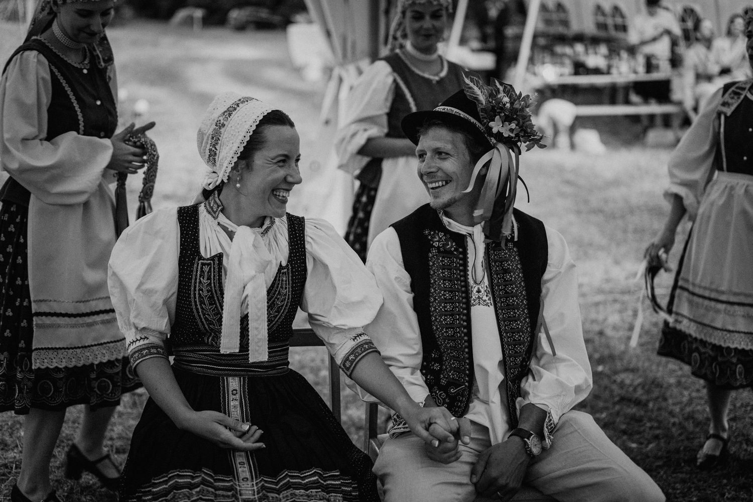Two women in traditional folk costumes laughing together at a cultural festival in black and white.