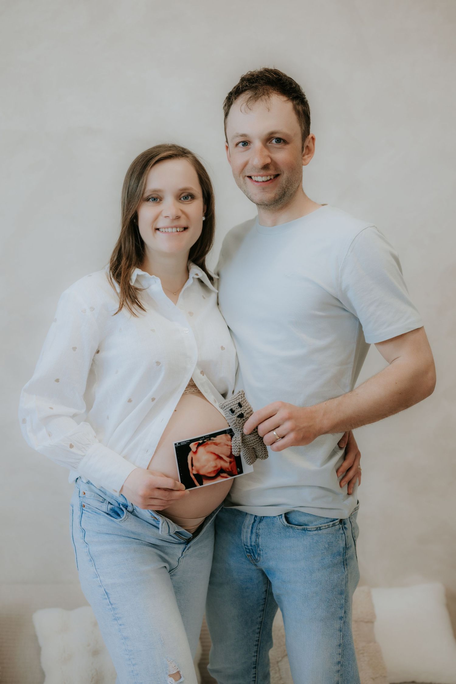 Smiling expectant couple holding ultrasound photo while posing together against neutral background.