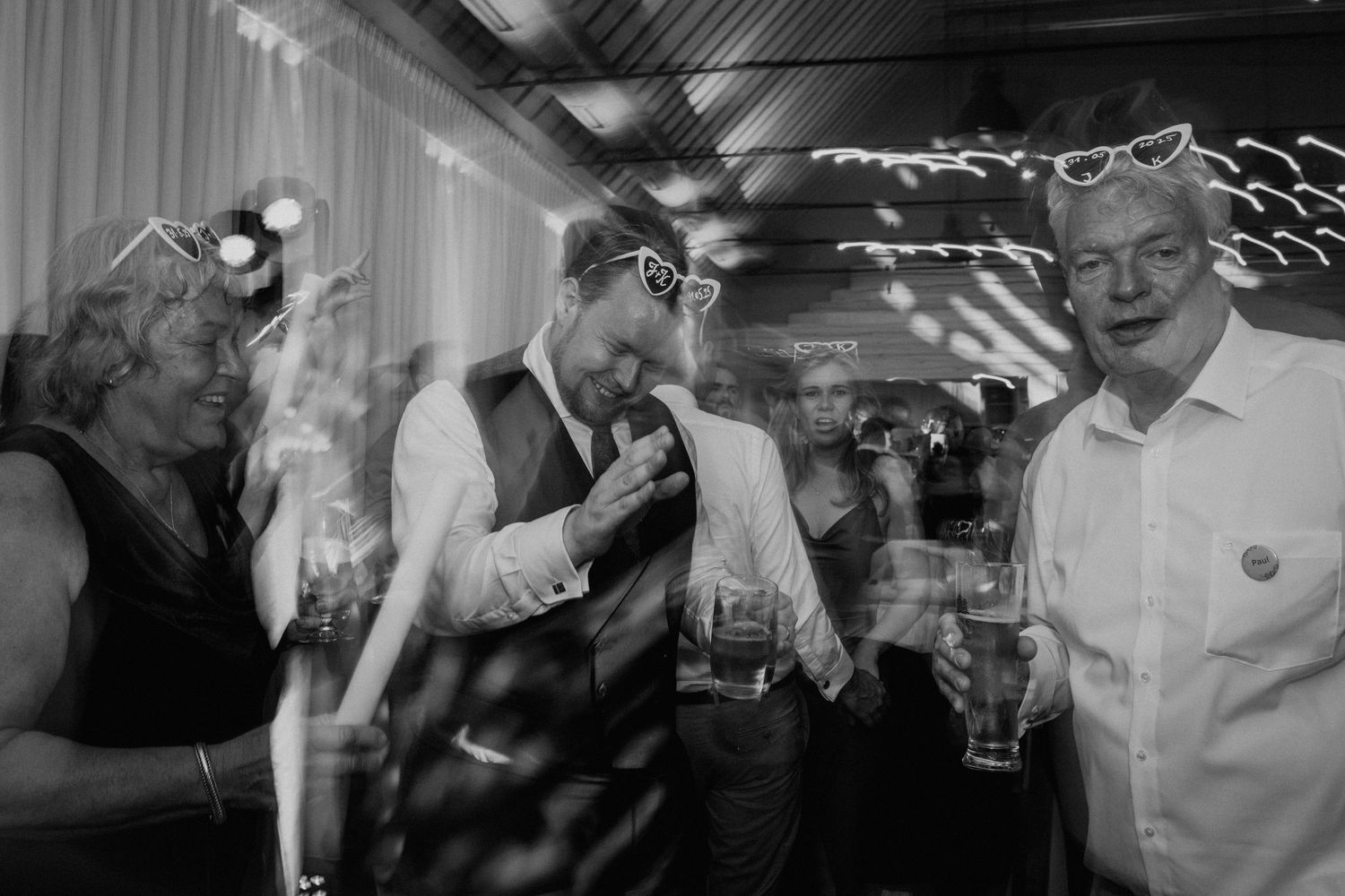 Black and white photo of wedding guests laughing and drinking at a lively reception party celebration.