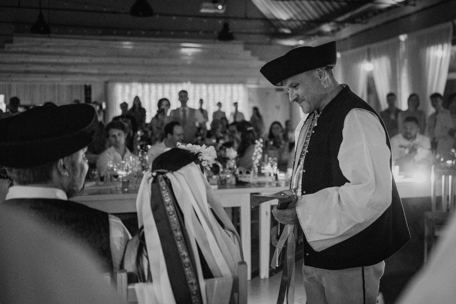 Black and white photo of men in traditional folk costumes at a wedding reception ceremony.
