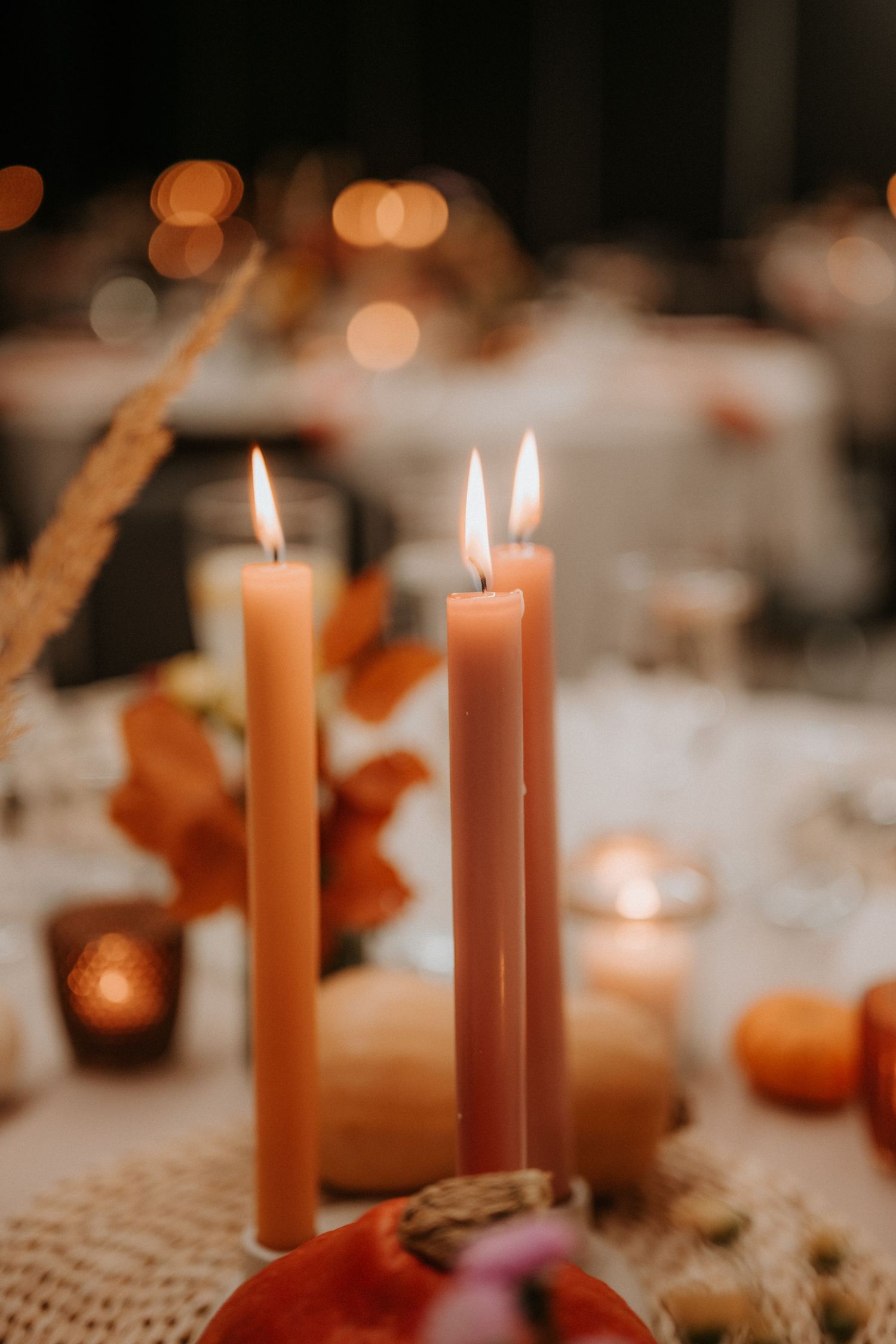 Two lit taper candles in warm autumn tones on a decorated table with bokeh lights and fall foliage.