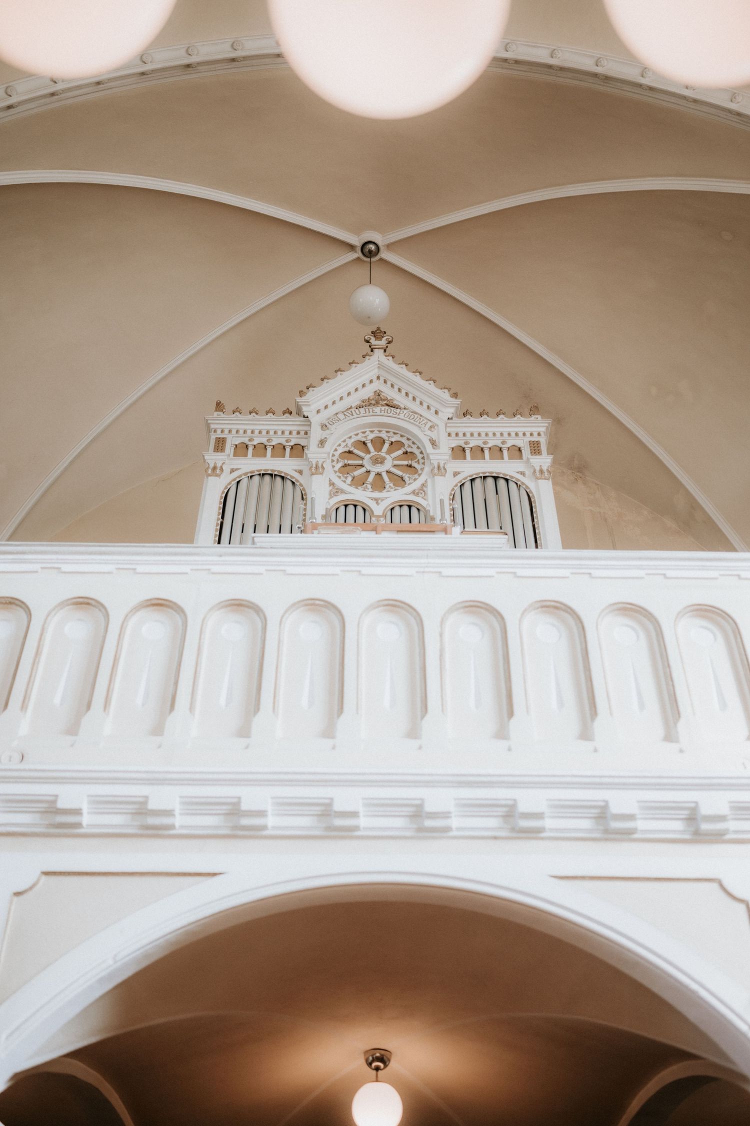 White church interior with ornate pipe organ loft featuring rose window and arched ceiling.