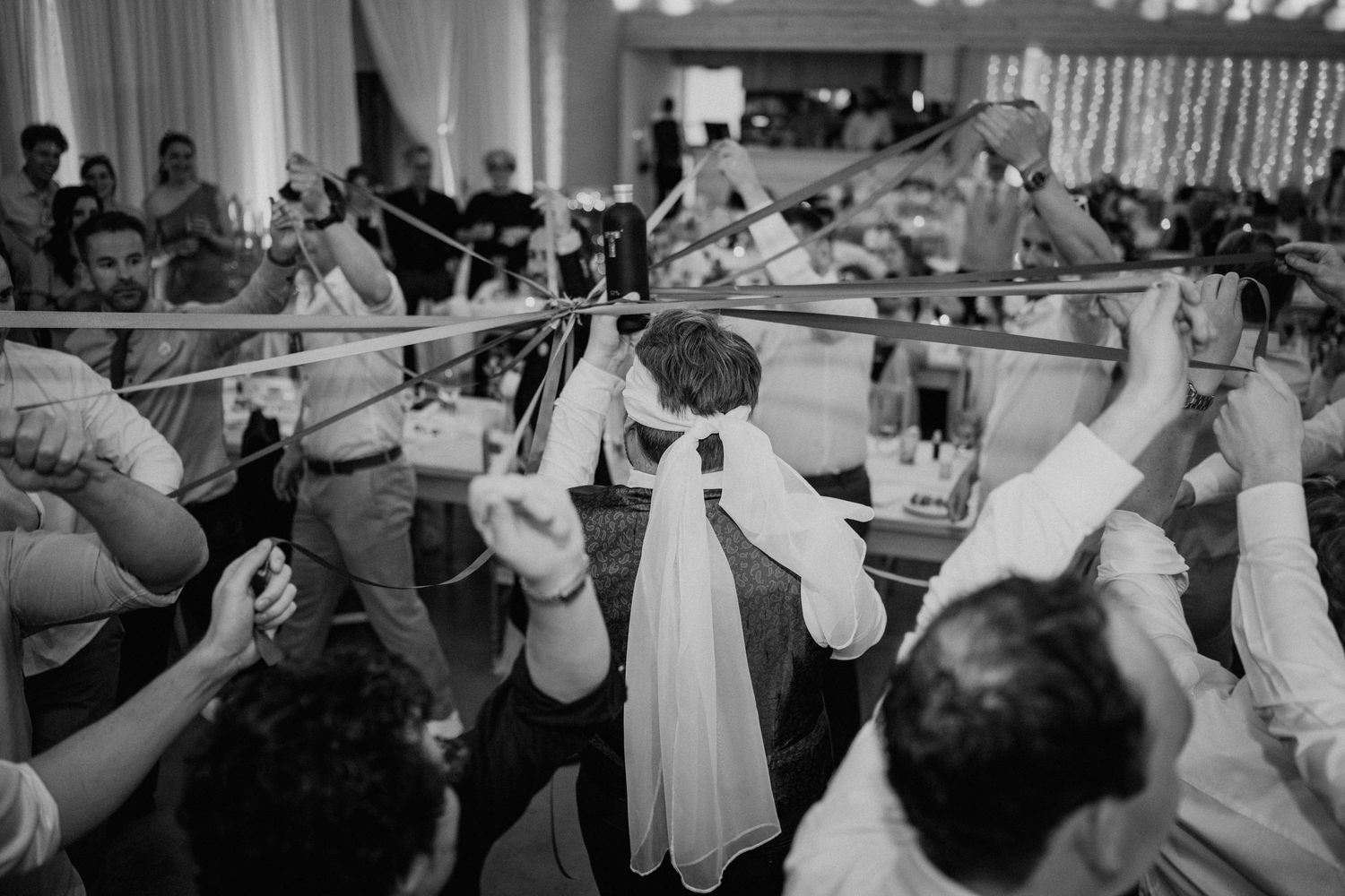 Black and white wedding reception photo of guests dancing under ribbons and streamers at a lively celebration.