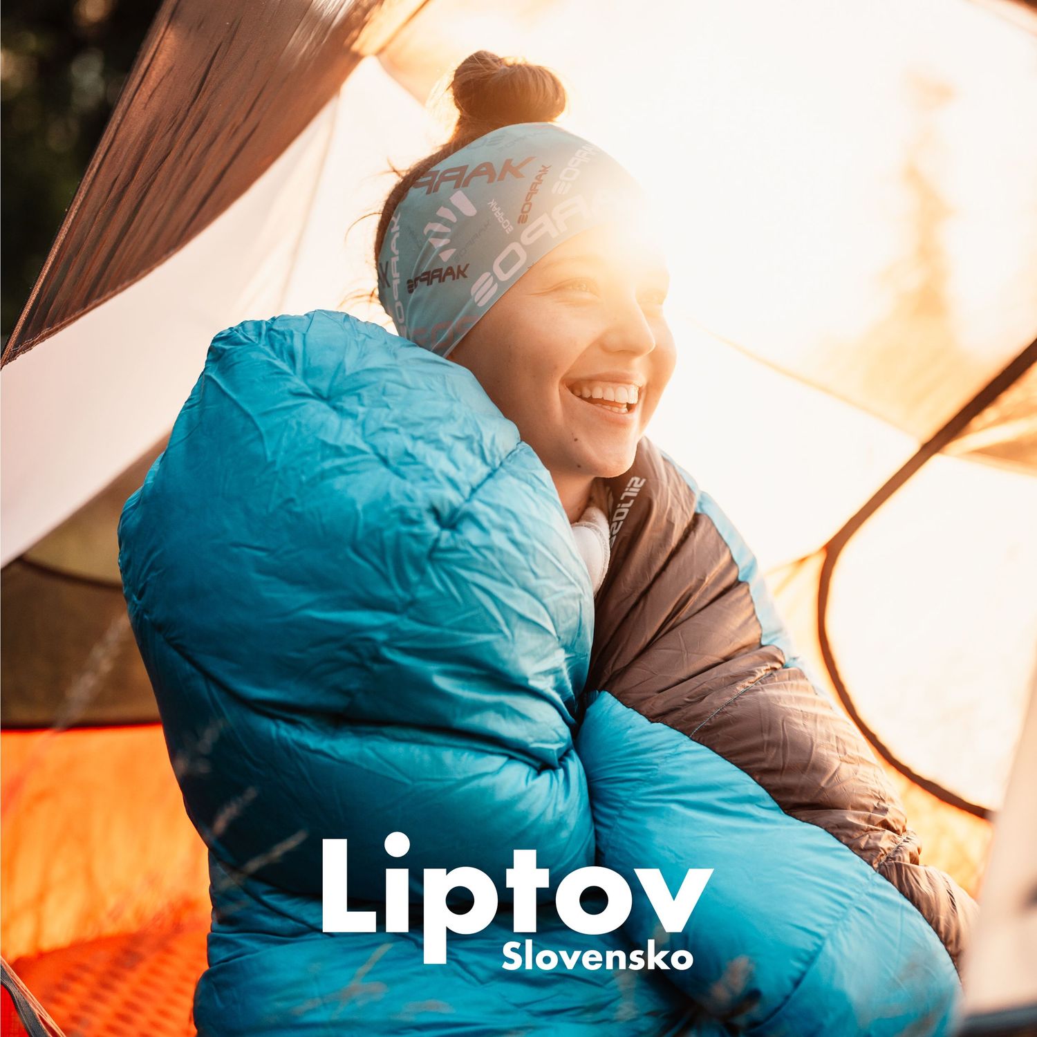 Happy woman in blue sleeping bag smiling inside a tent during winter camping in Liptov, Slovakia.