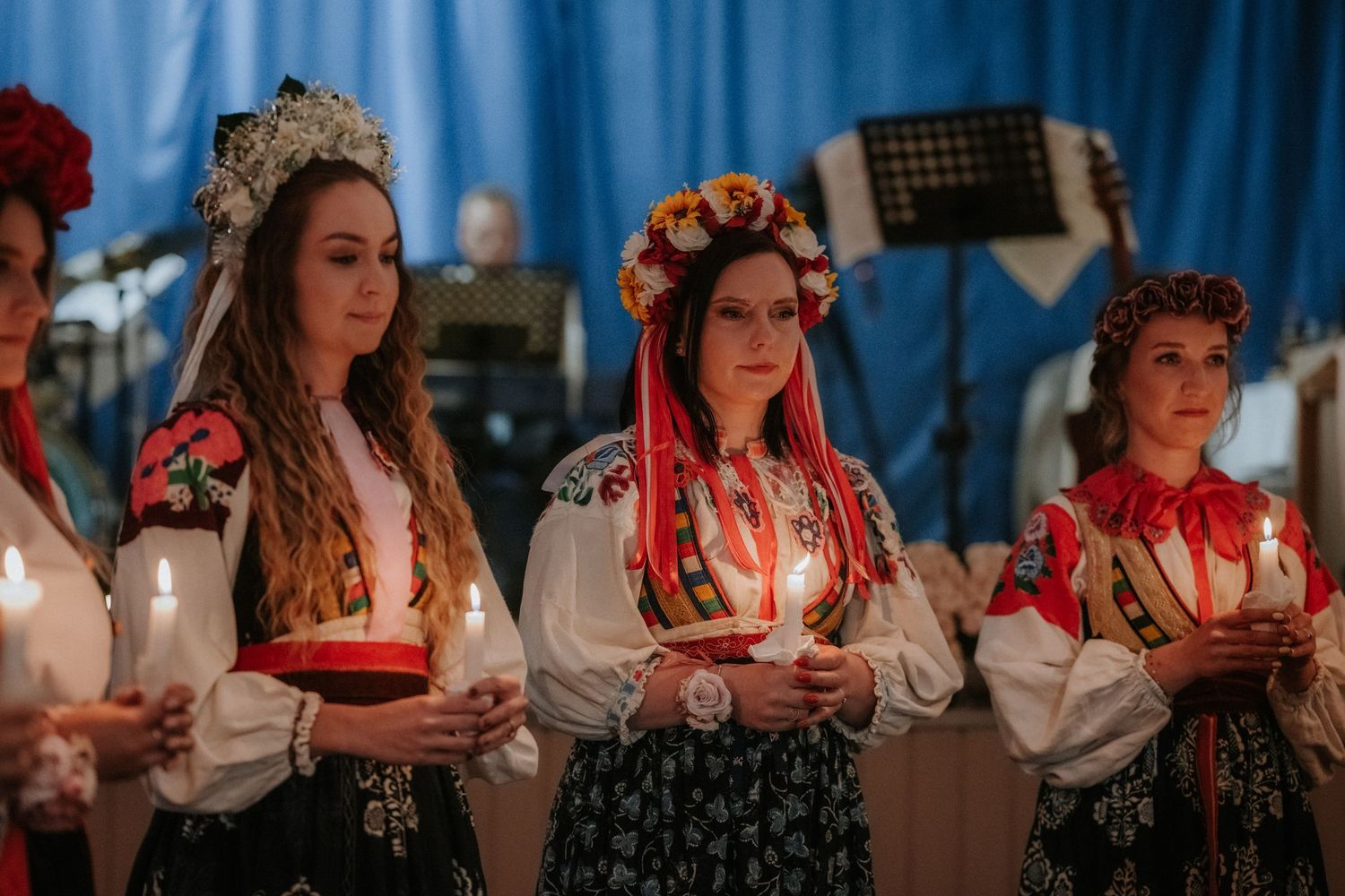Women in traditional Ukrainian embroidered costumes holding candles at a cultural folk festival ceremony.