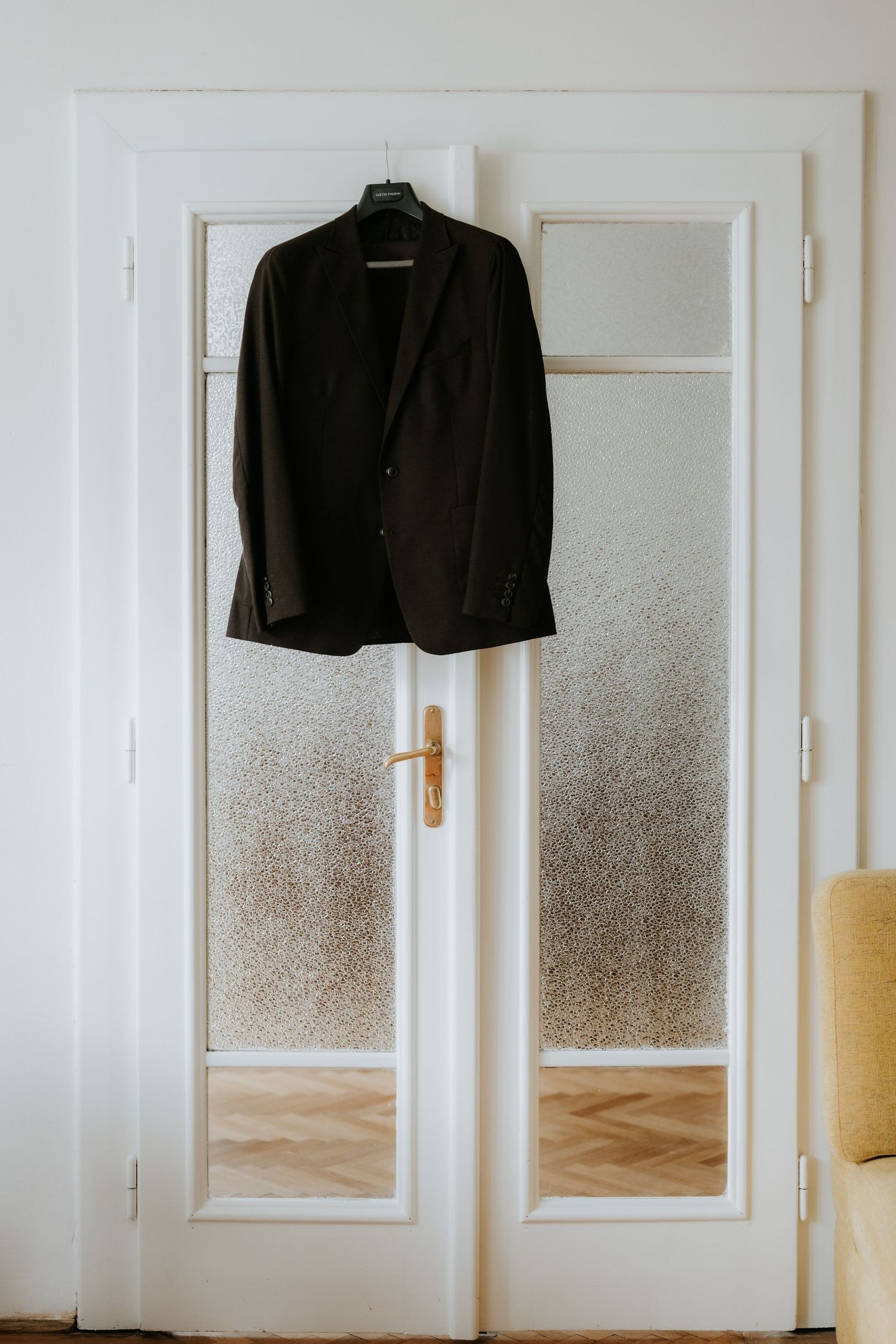 A dark suit jacket hanging on a hanger over a white door with frosted glass panels and gold handle.