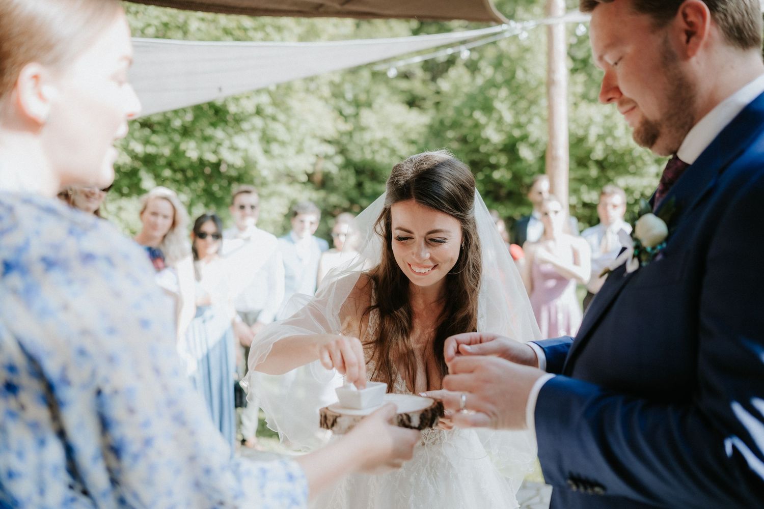 Bride and groom exchanging wedding rings during an outdoor ceremony, smiling joyfully.