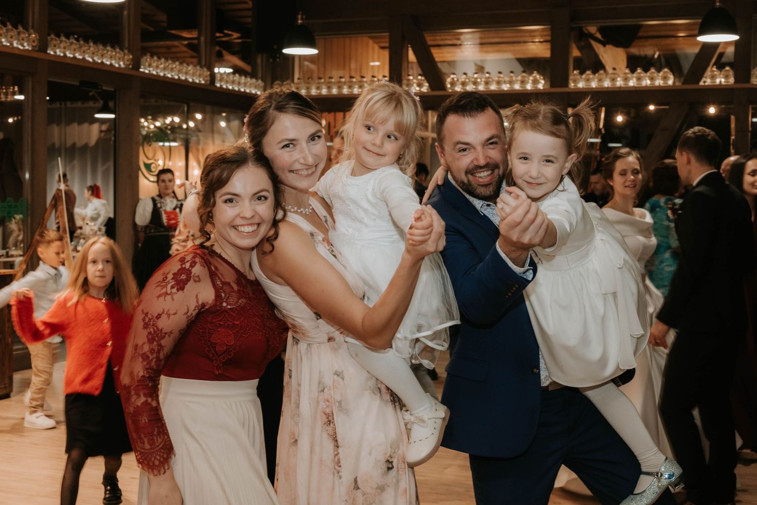 Happy wedding family portrait with bride, groom, and two young children dancing at reception.