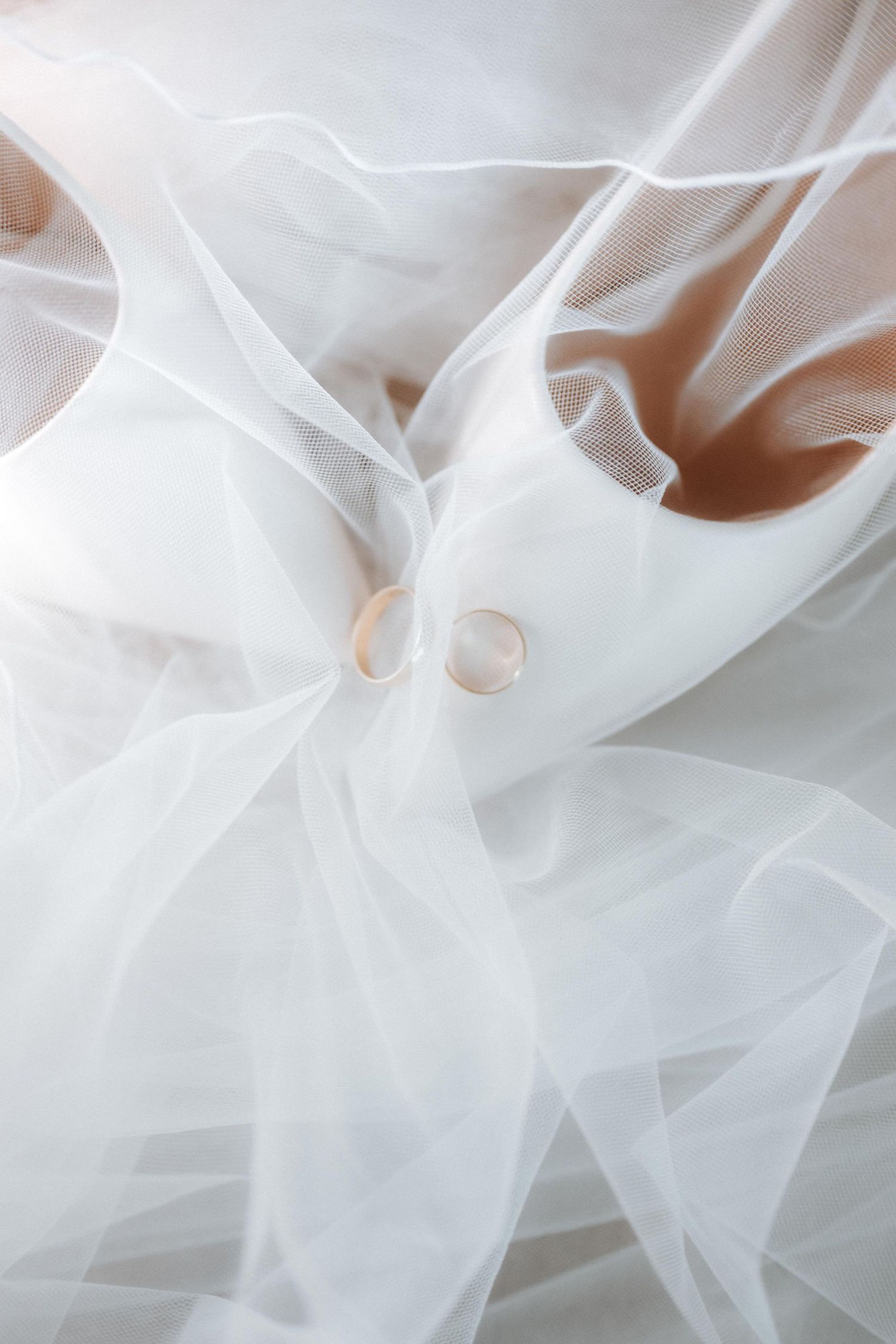 White bridal heels with two gold wedding bands on sheer tulle veil.