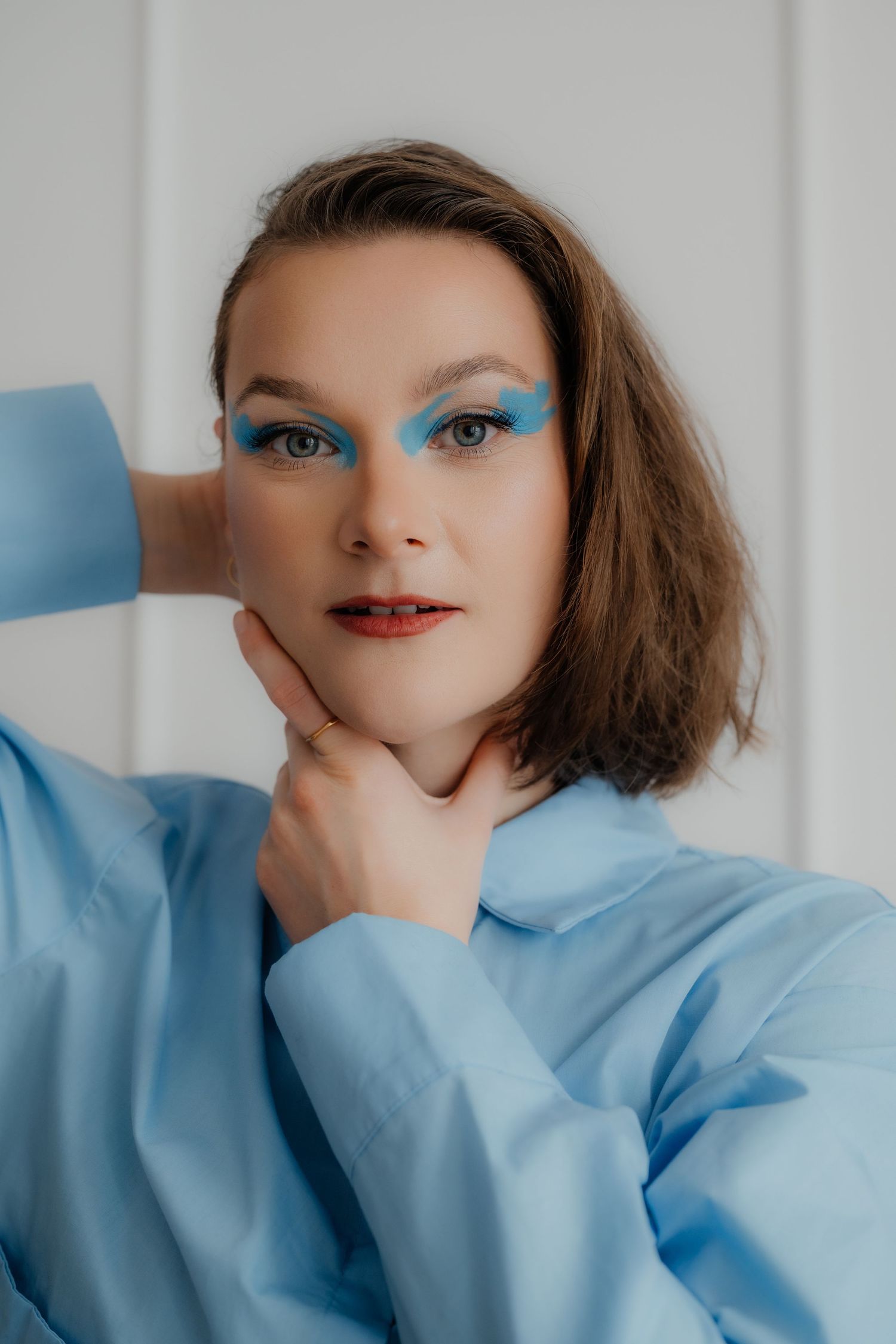 Portrait of woman with dramatic blue eyeshadow in light blue oversized shirt posing.