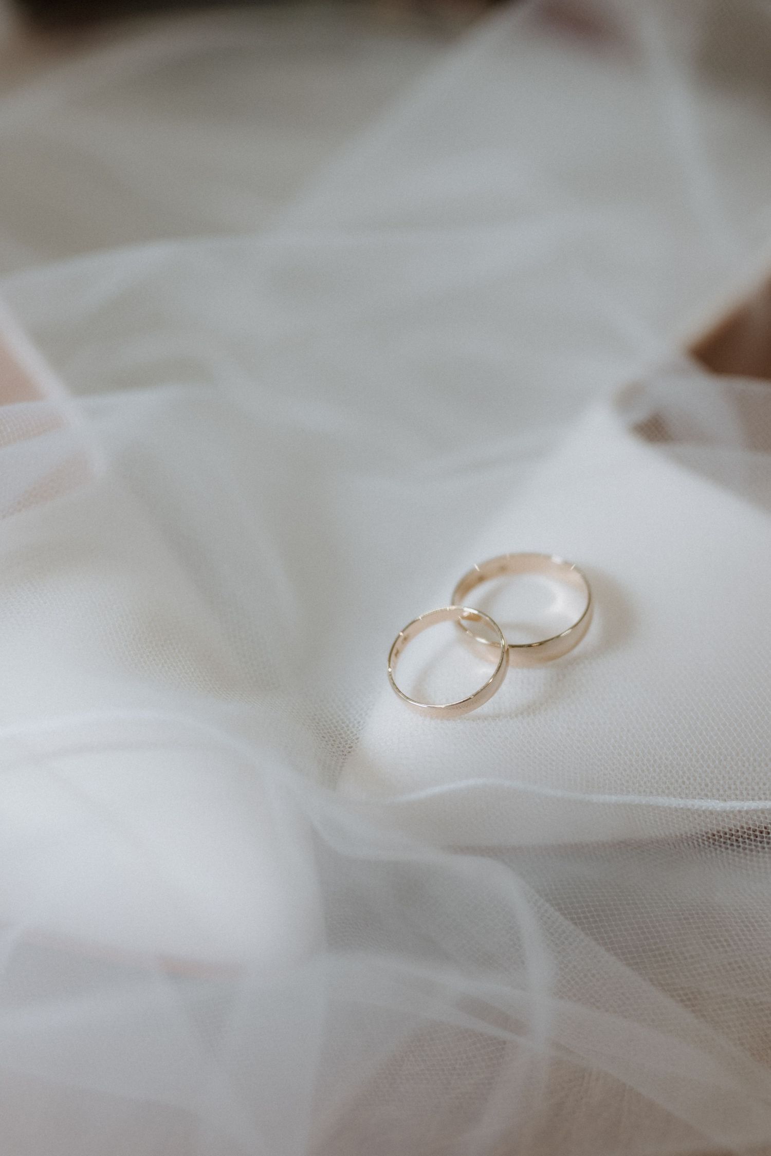 Two gold wedding bands resting on soft white bridal veil fabric, symbolizing marriage and eternal love.