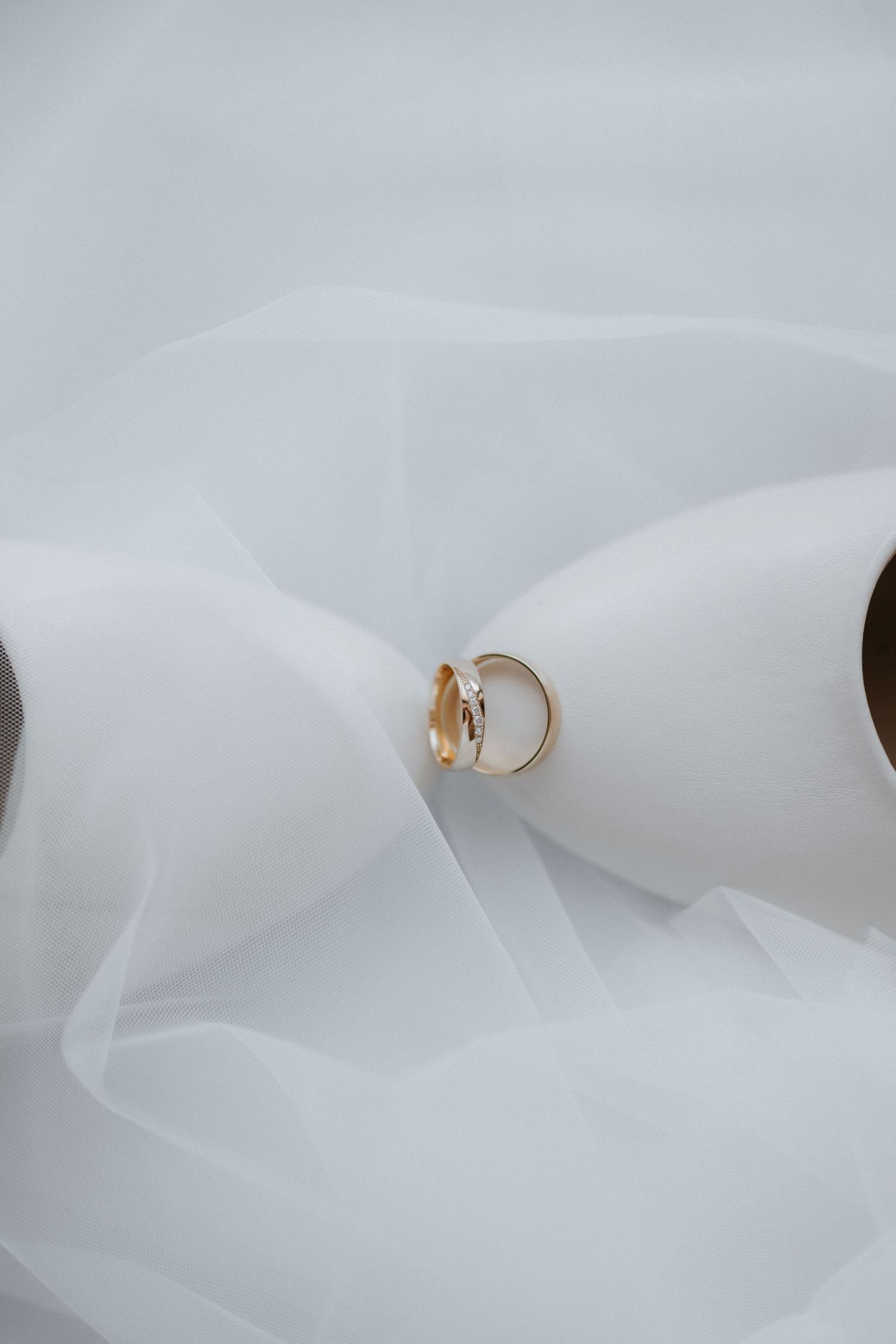 Gold wedding ring with diamond resting on white tulle fabric, elegant bridal jewelry detail photography.