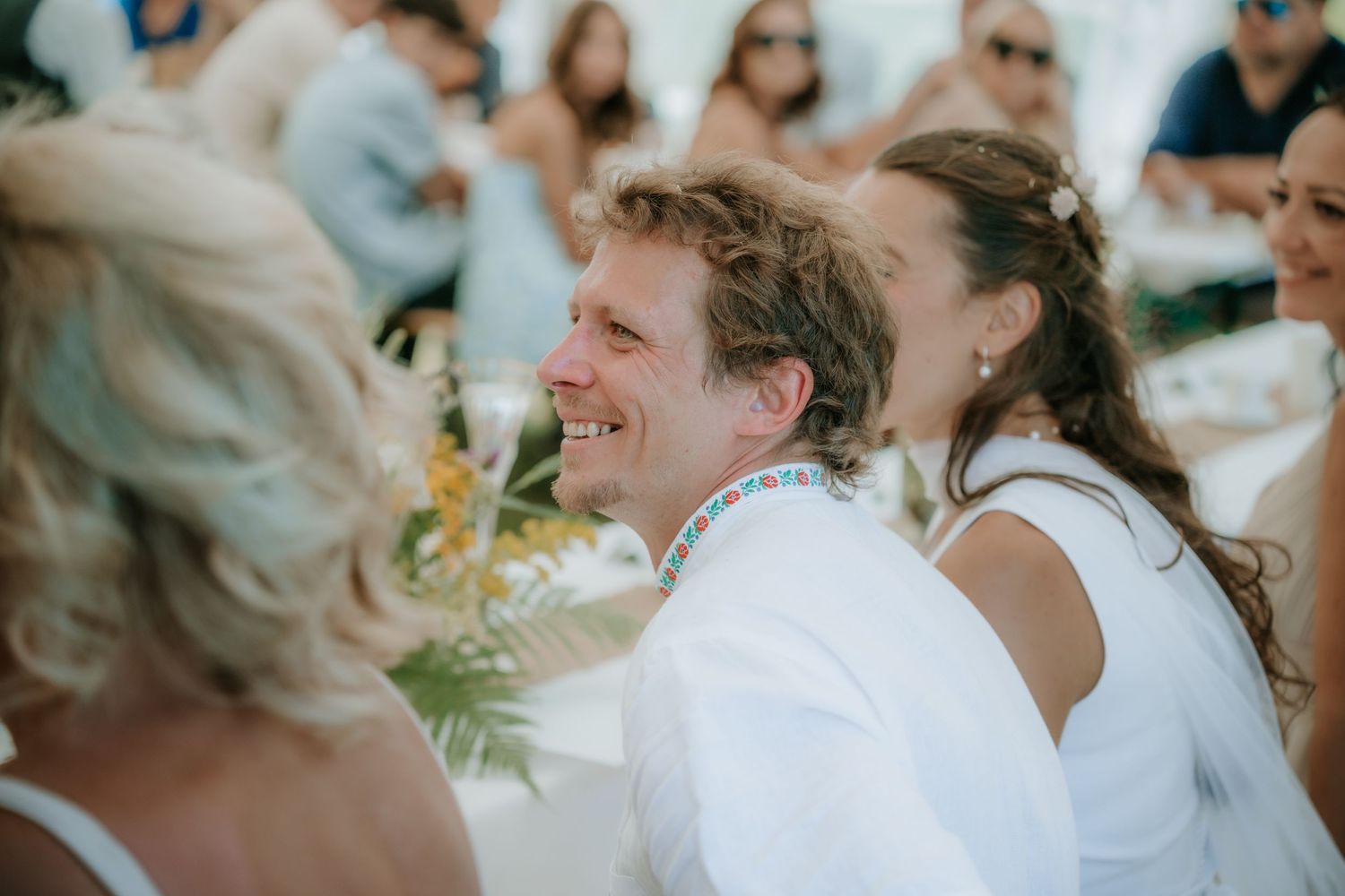 Smiling man and woman in white attire at an outdoor beach wedding reception celebration.