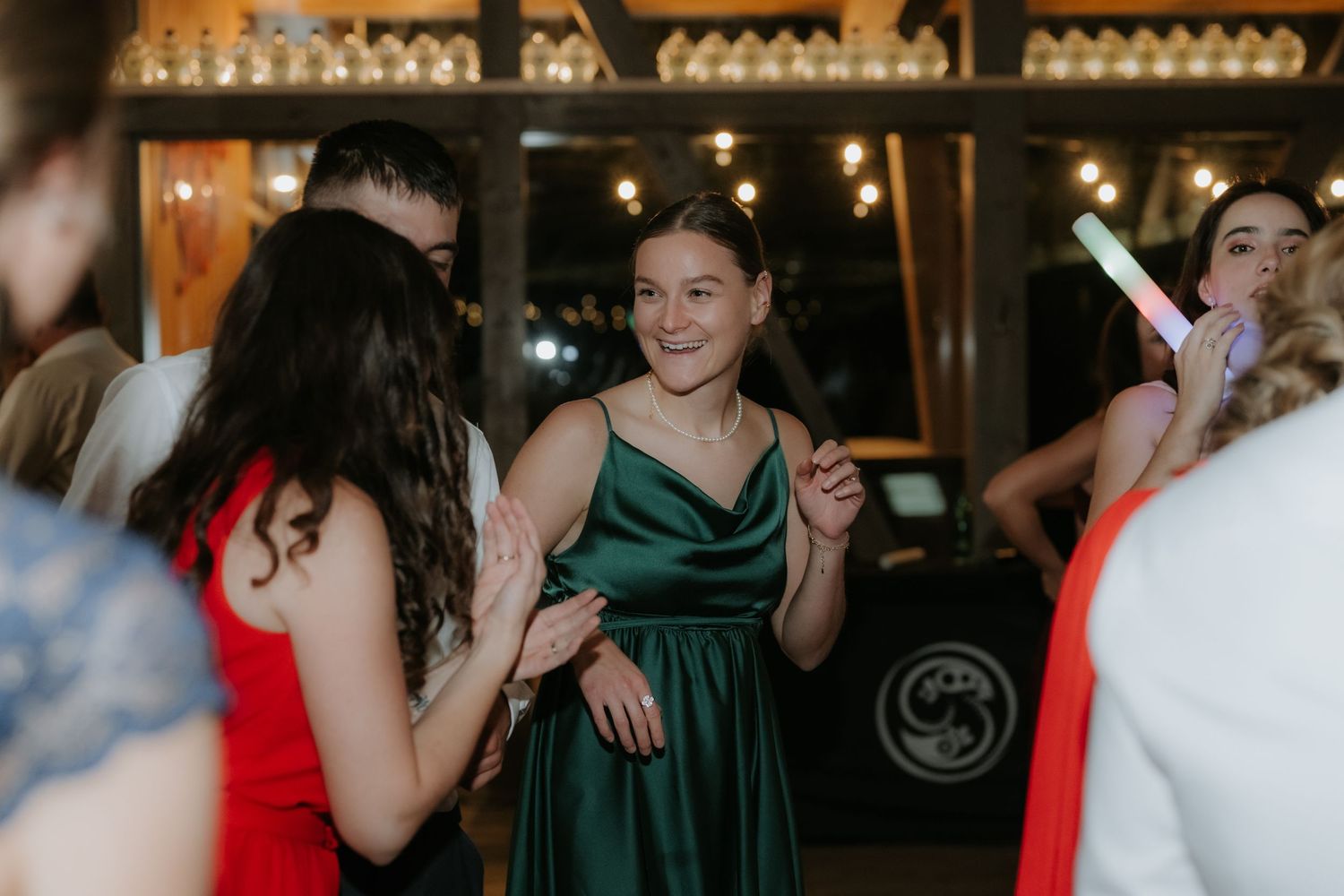 Young woman in elegant green satin dress dancing and smiling at a formal event with string lights.