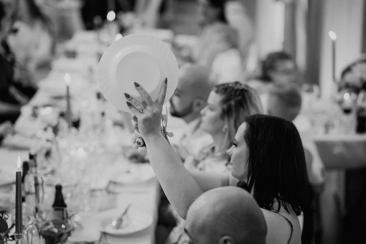Black and white photo of a woman raising a white plate at an elegant dinner party reception.