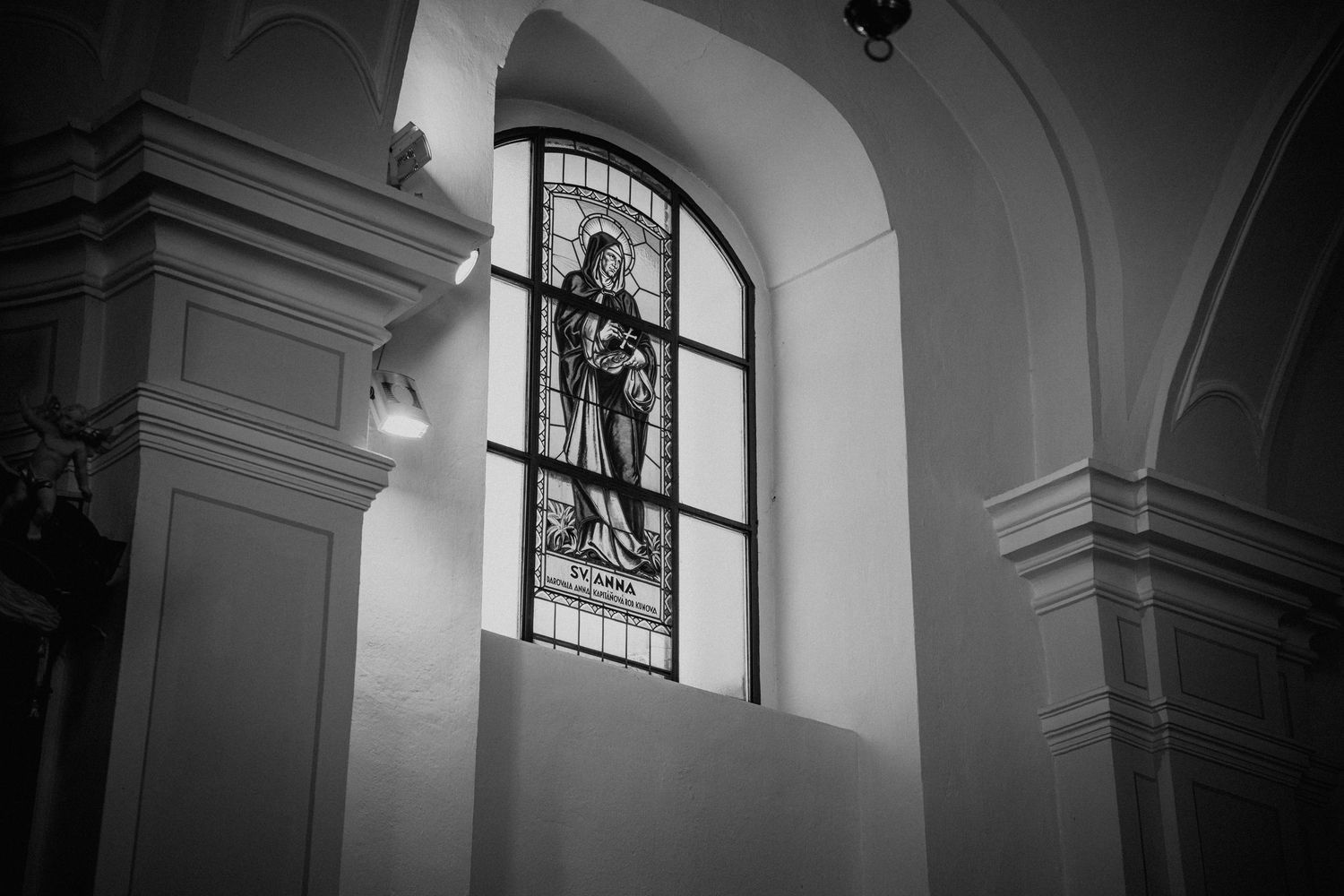 Black and white photo of a stained glass window depicting a saint figure inside an ornate church interior.