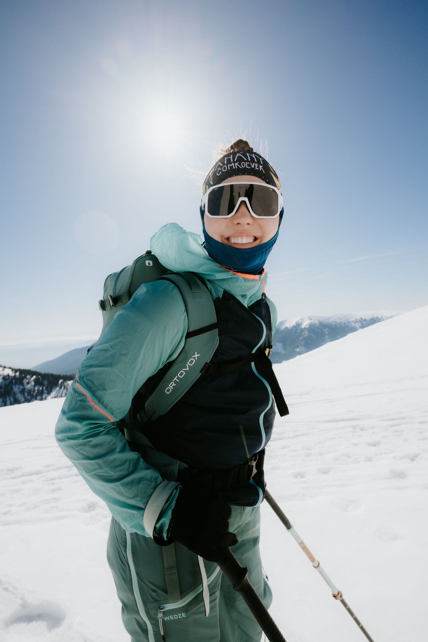 Close-up portrait of a female skier wearing Ortovox backpack and goggles on a sunny snowy mountain.