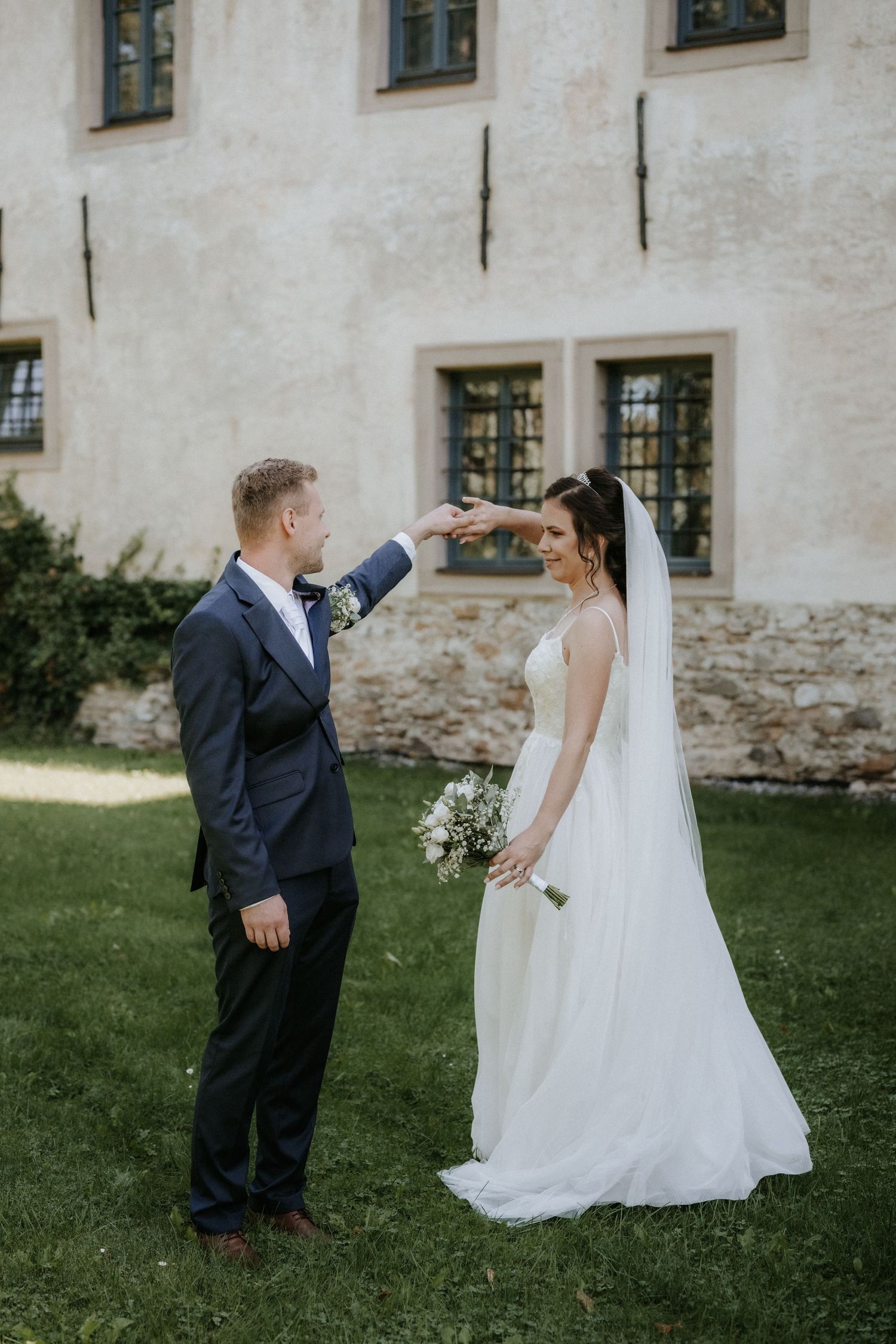 Groom spinning bride in white gown outside a historic stone building on their wedding day.