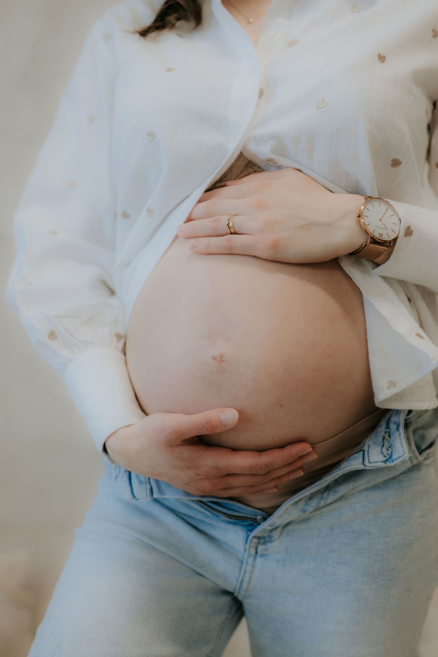 Close-up of a pregnant woman in a white shirt and jeans gently holding her bare baby bump.