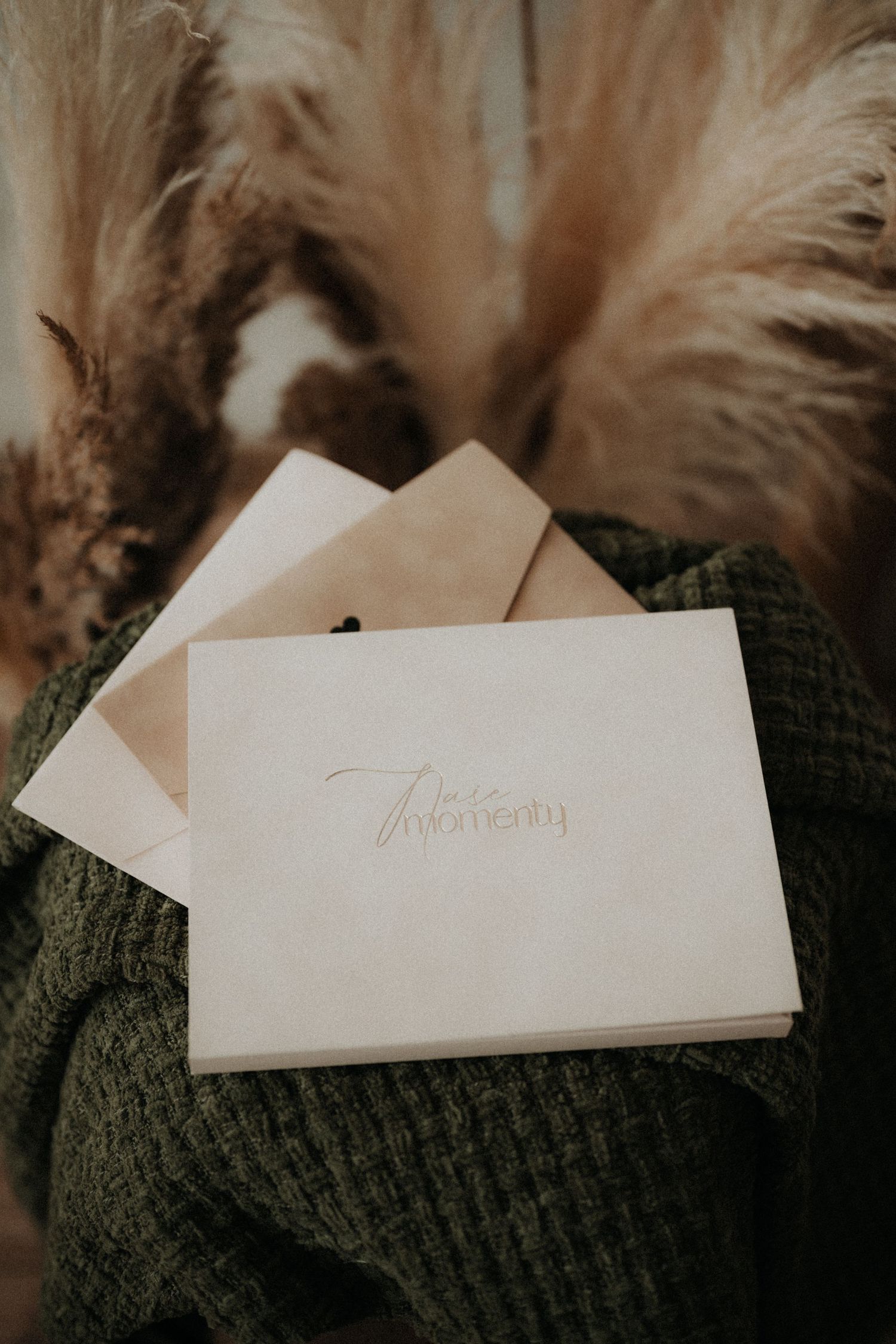 A cream wedding vow book with cursive text rests on a green knit sweater with pampas grass in the background. Liptovský Mikuláš