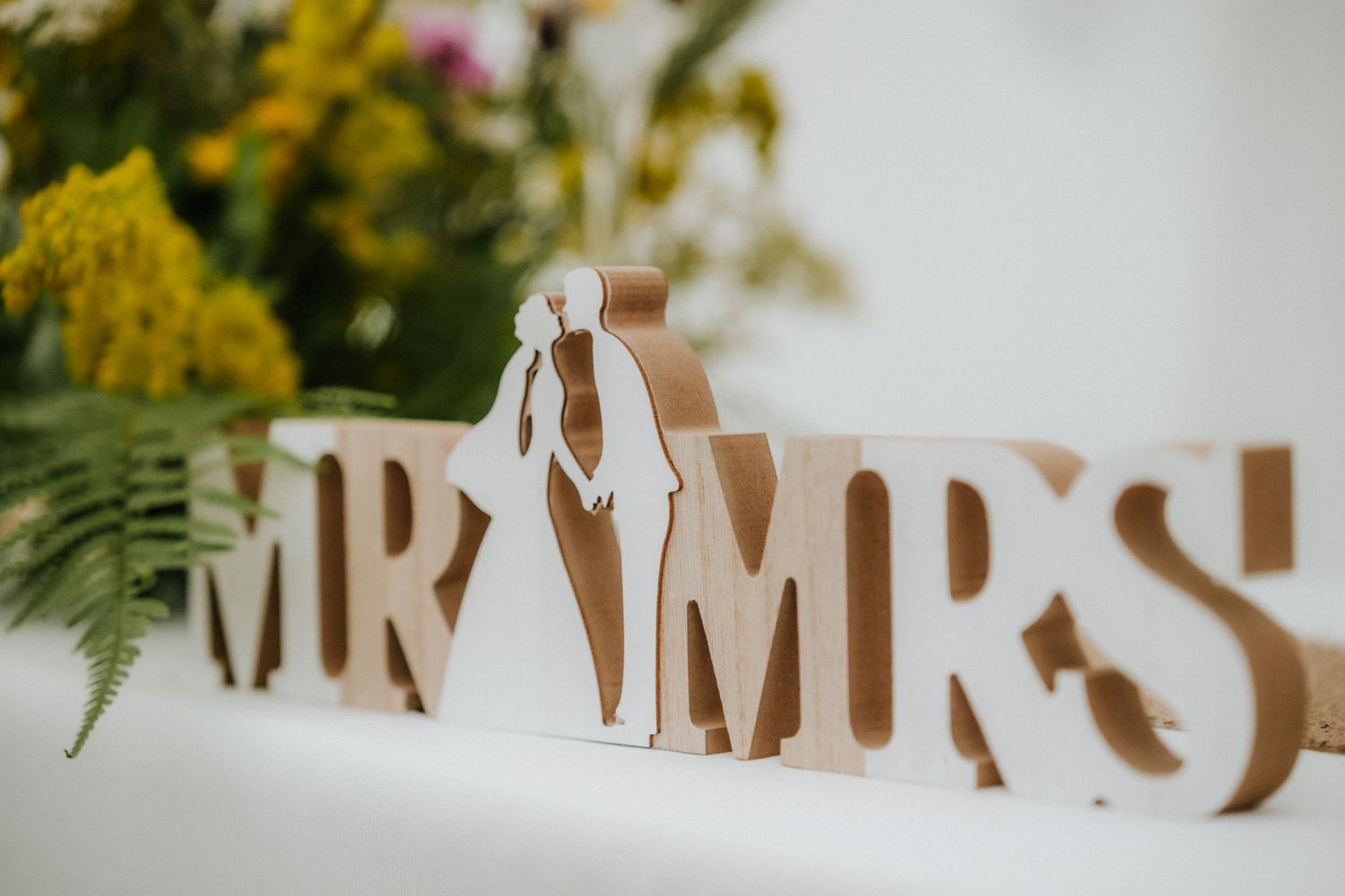 Wooden MR and MRS wedding sign with bride and groom silhouette, surrounded by colorful flowers and greenery.