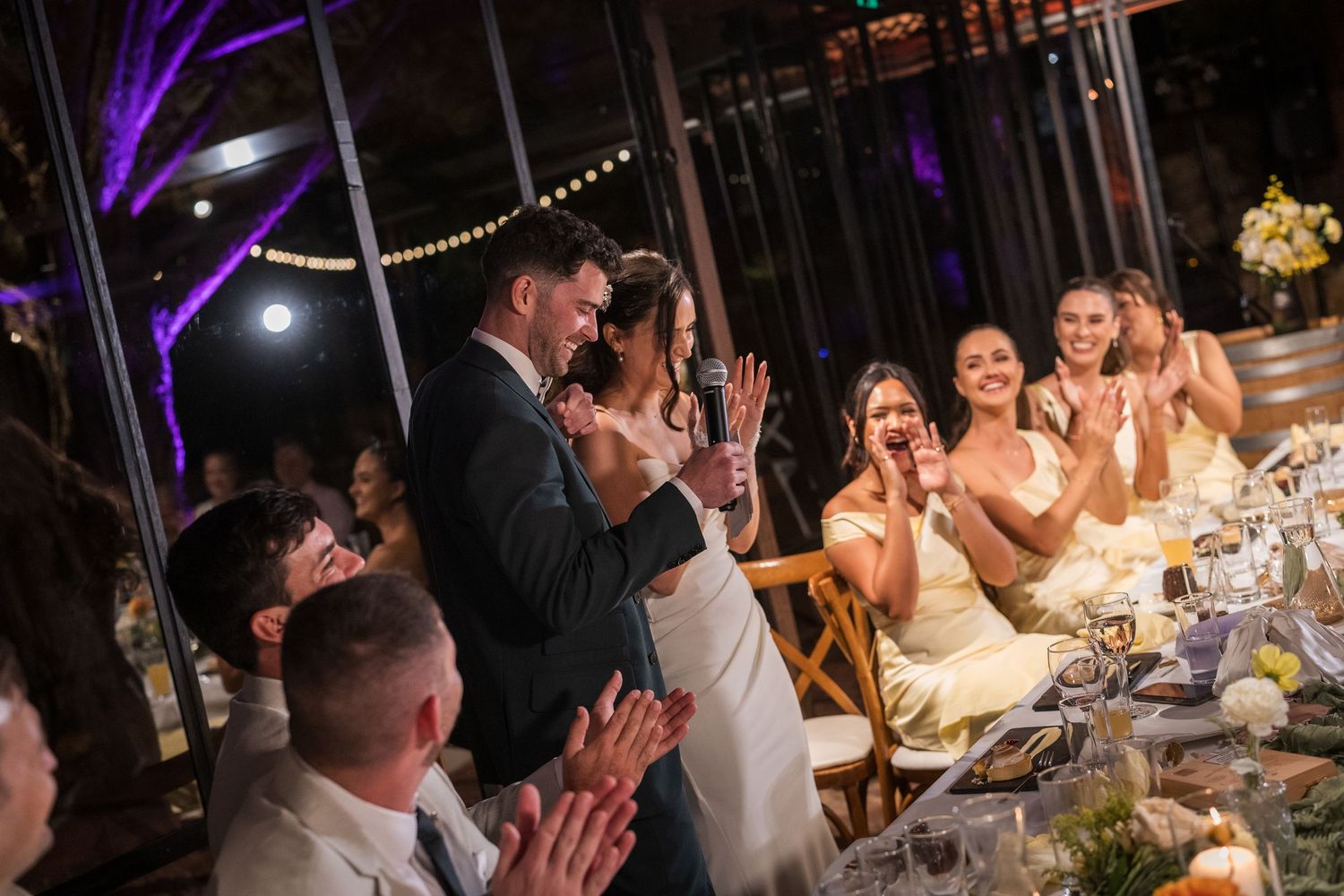 Bride and groom share romantic first dance while wedding guests applaud at evening reception.