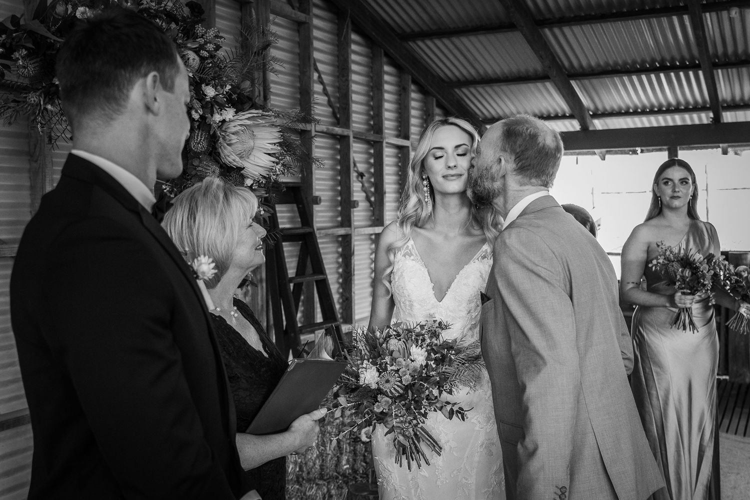 Wedding ceremony in progress inside rustic barn setting with natural light.