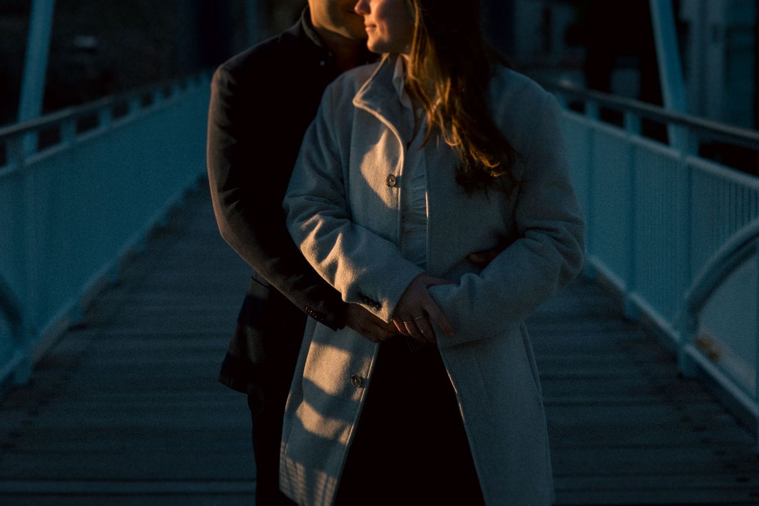 A tender moment shared on a wooden boardwalk at dusk with dramatic lighting.