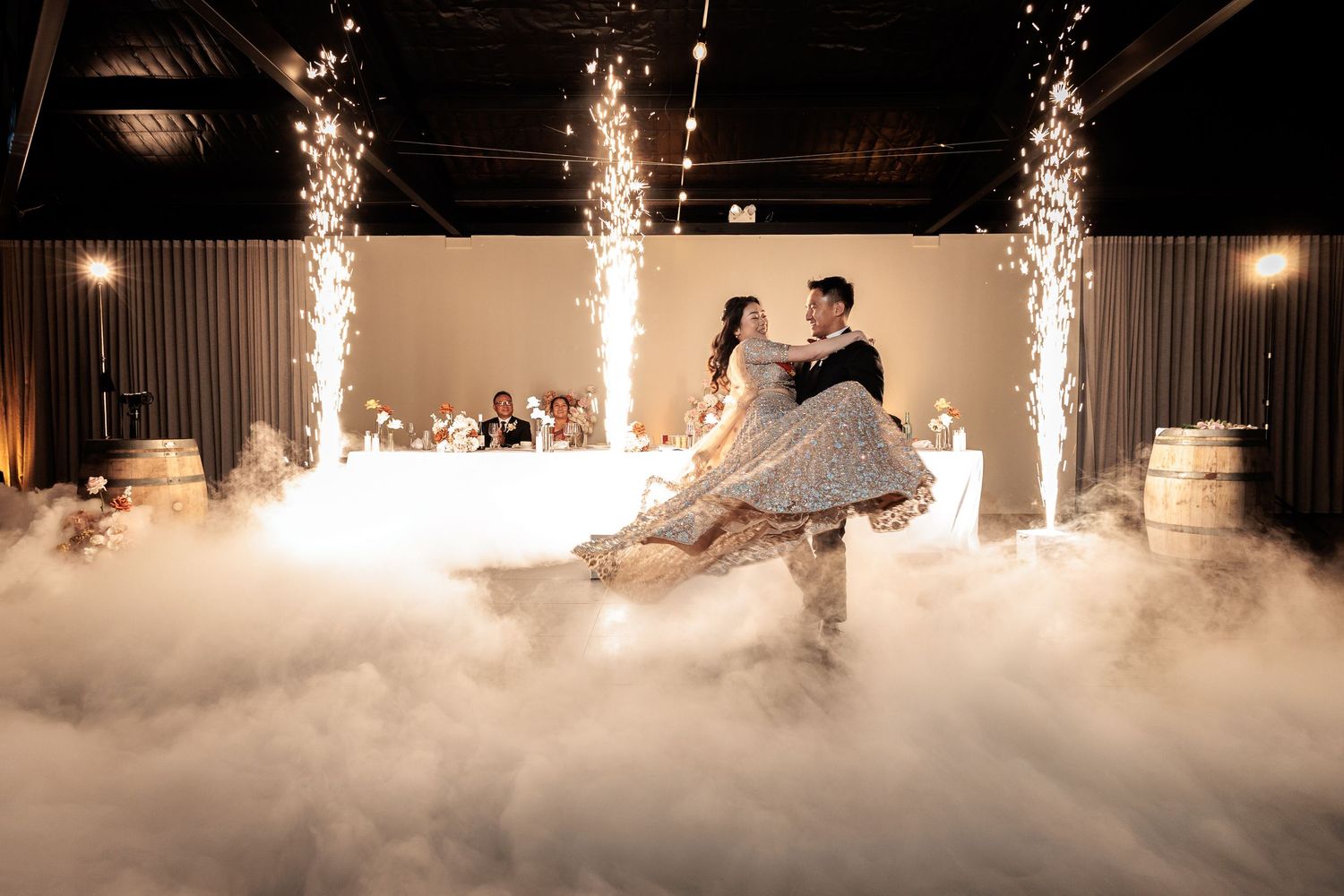 Couple shares first dance surrounded by sparkling cold sparklers and romantic fog on wedding dance floor.